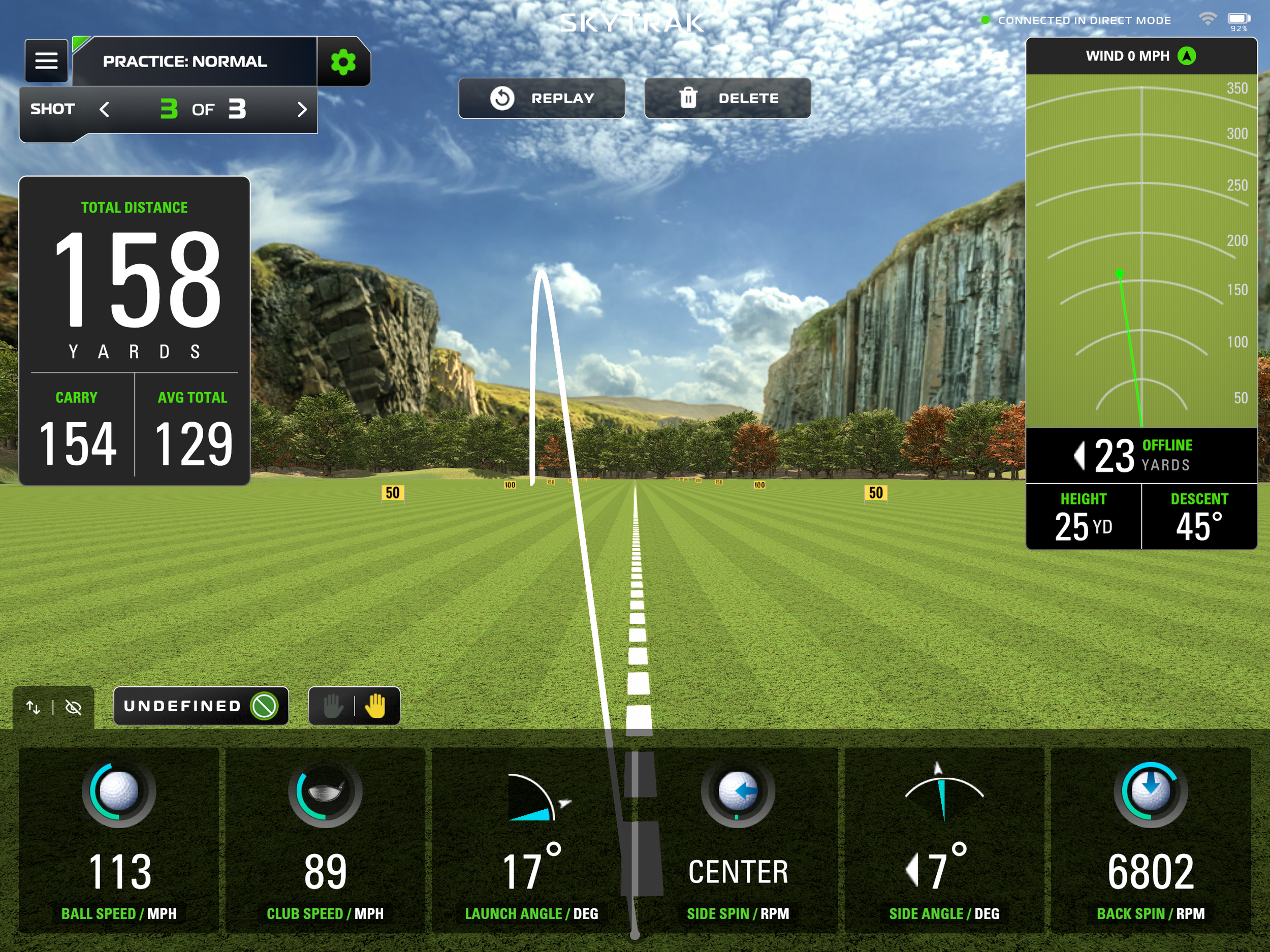 Golf driving range with trees, mountains, and a bright blue sky with clouds. The screen displays golf practice data such as total distance, carry, average total, and shot parameters like ball speed, club speed, launch angle, and spin rate.