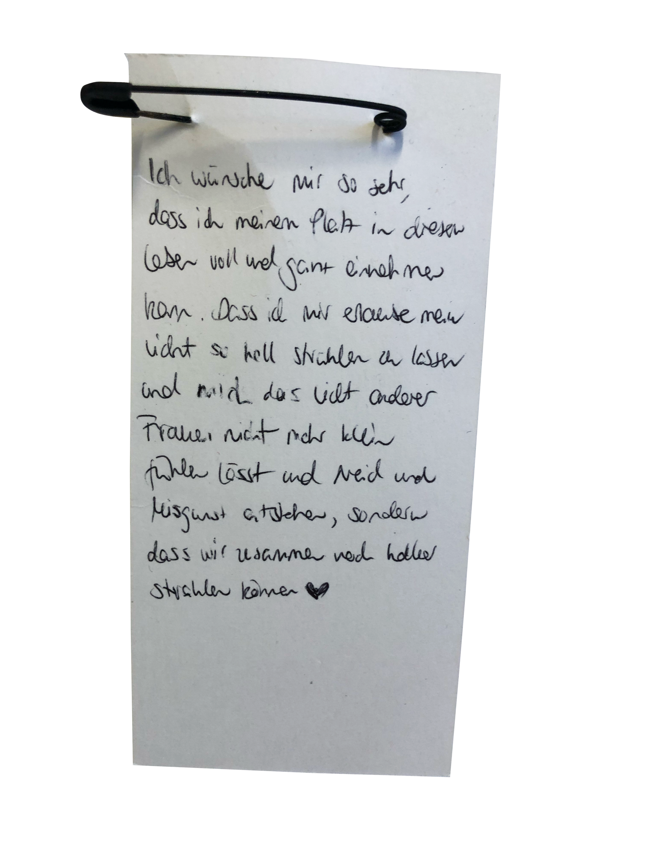 A handwritten note in German on a piece of white paper pinned with a black safety pin.
