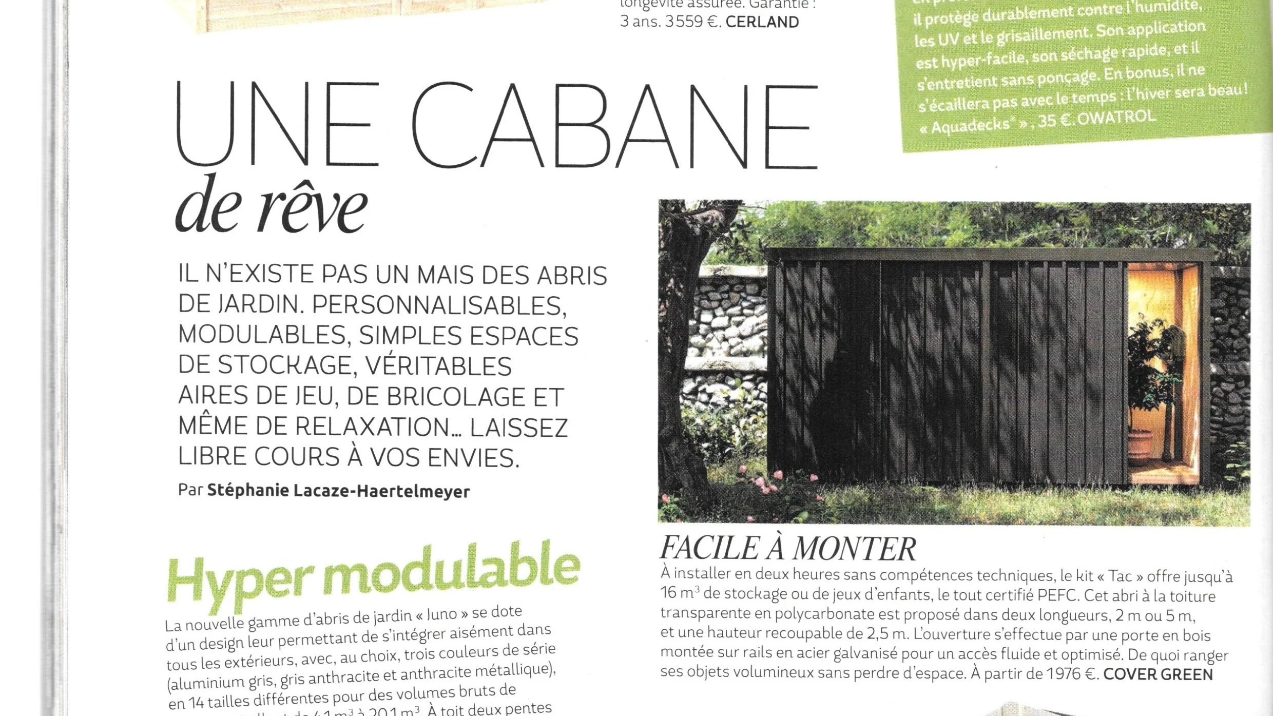 Une photo d'une petite cabane en bois noire dans un jardin avec des arbres et des plantes, vue de face, avec une porte entrouverte illuminée à l'intérieur.