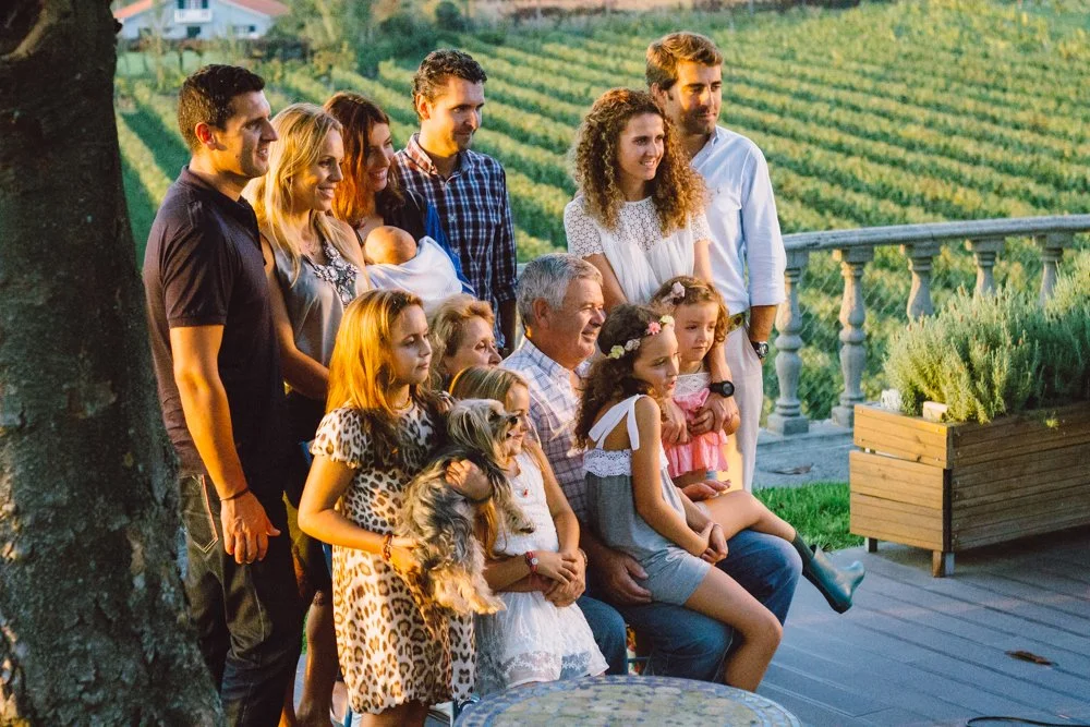 Família se reúne ao ar livre em um jardim com vista para campos verdes, posando para uma foto comemorativa.