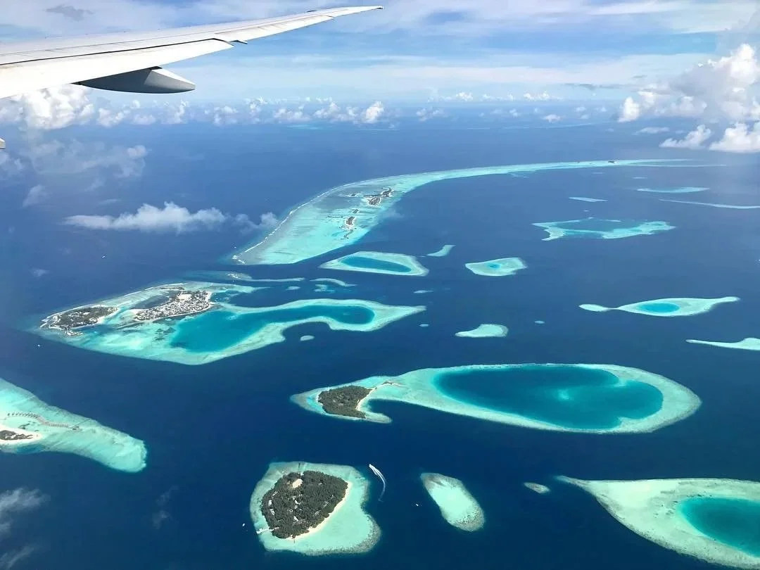 Aerial view of the Maldives with turquoise lagoons and coral islands from an airplane window.