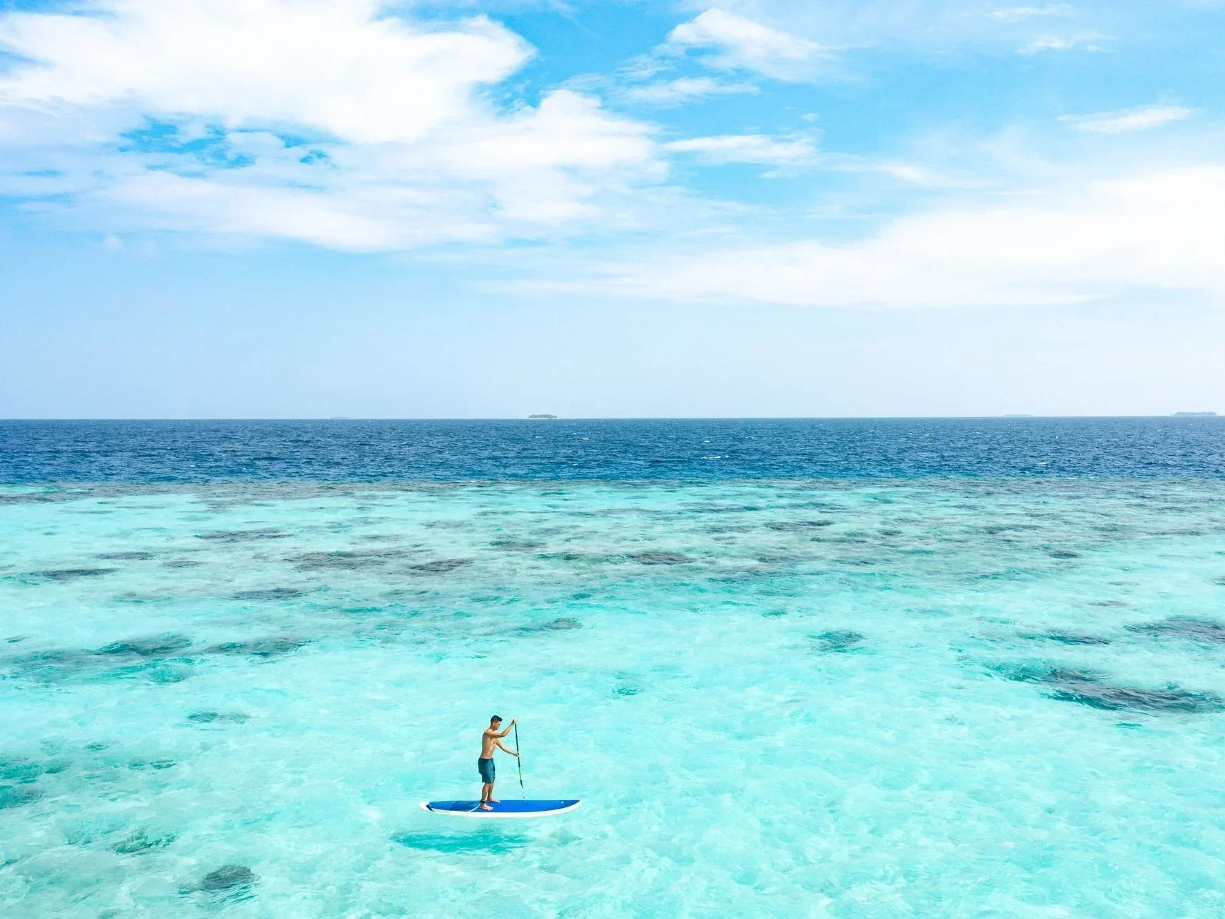 Person paddleboarding on clear turquoise water with a vast ocean and sky in the background