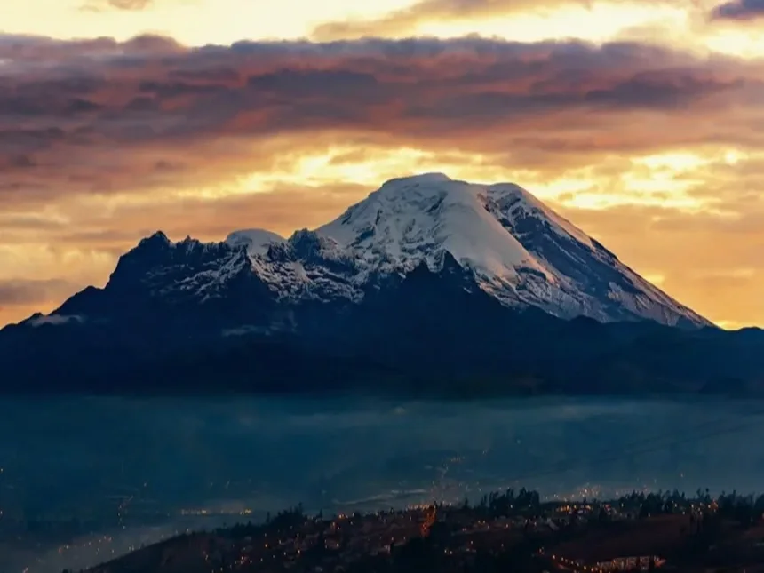 Snow-capped Mount Chimborazo at sunset with a colourful sky and a town at the base.