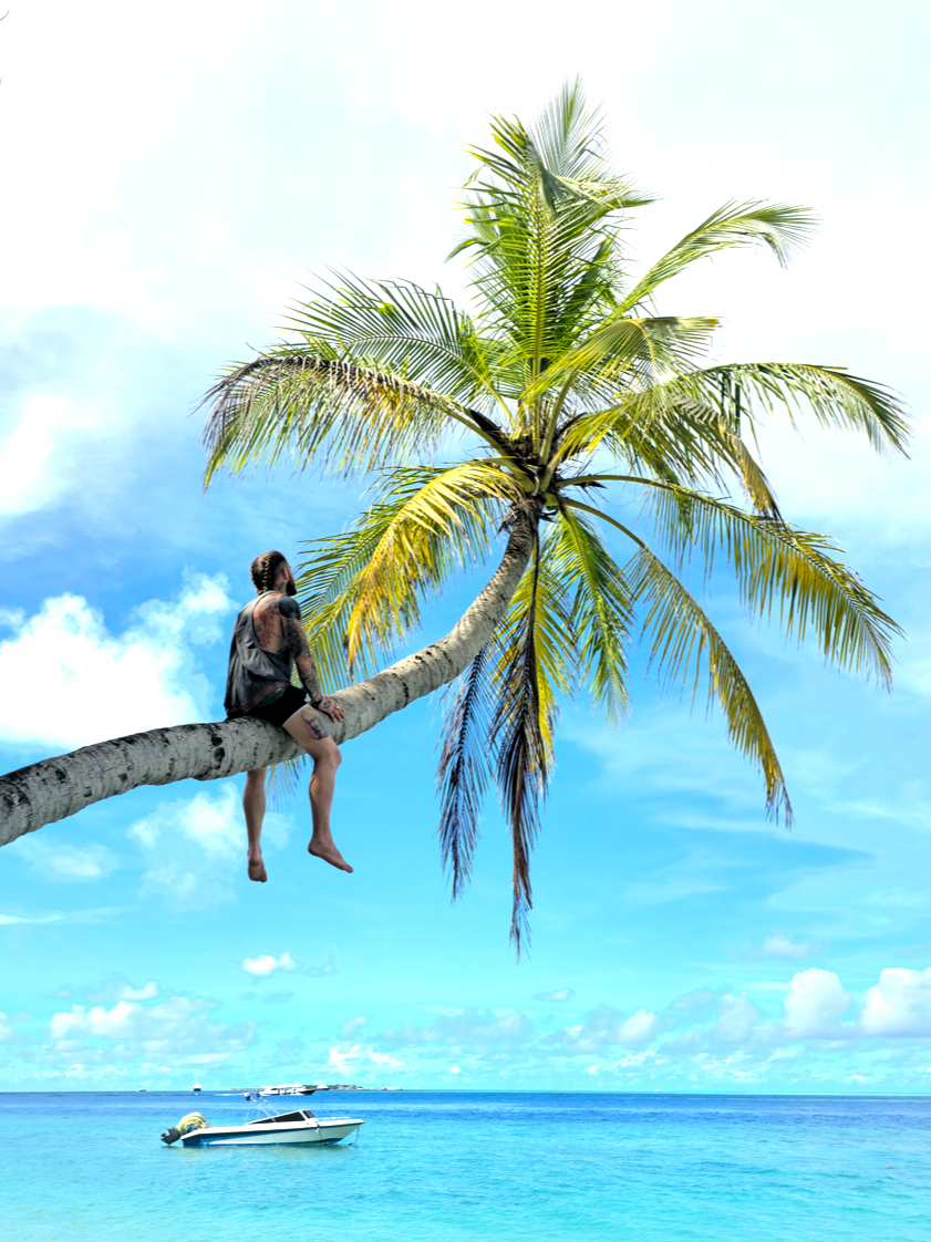 A person sitting on a leaning palm tree over the ocean with boats in the water and a partly cloudy sky.