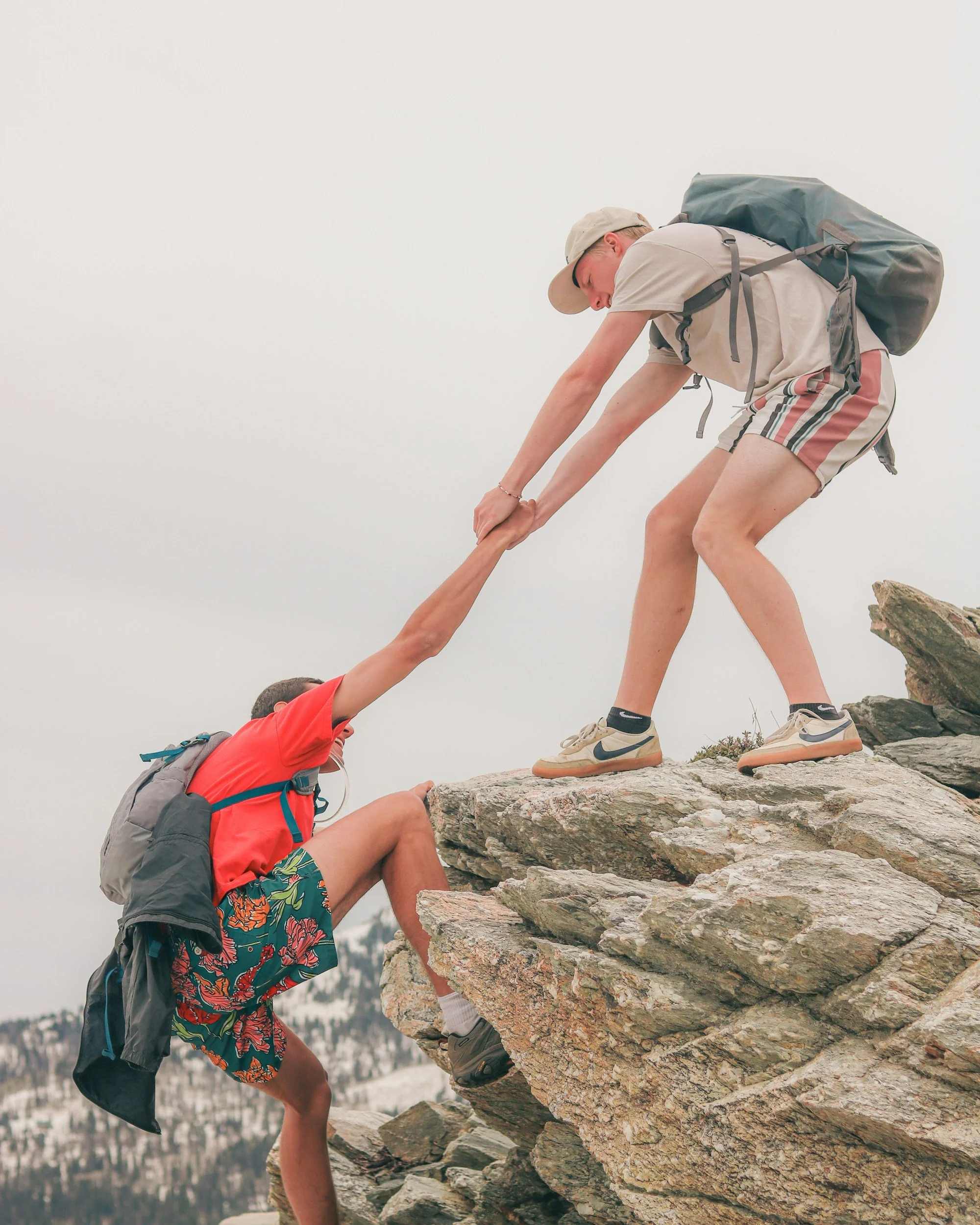 One hiker helping another climb rocks, representing guidance and support when taking the next step