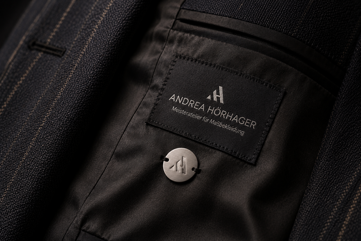 Innenansicht eines Maßanzuges mit einem Etikett von Andrea Hörhager, Meisteratelier für Maßbekleidung, und einem Knopf mit dem Logo 'AH'.