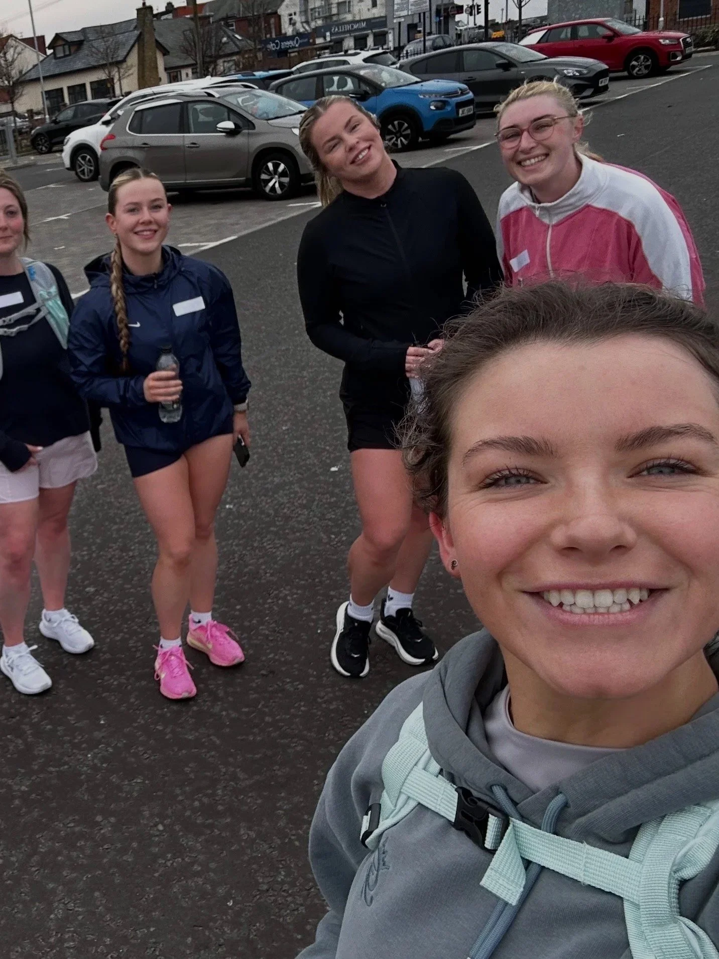 Group of young women smiling and taking a selfie outdoors in a parking lot.