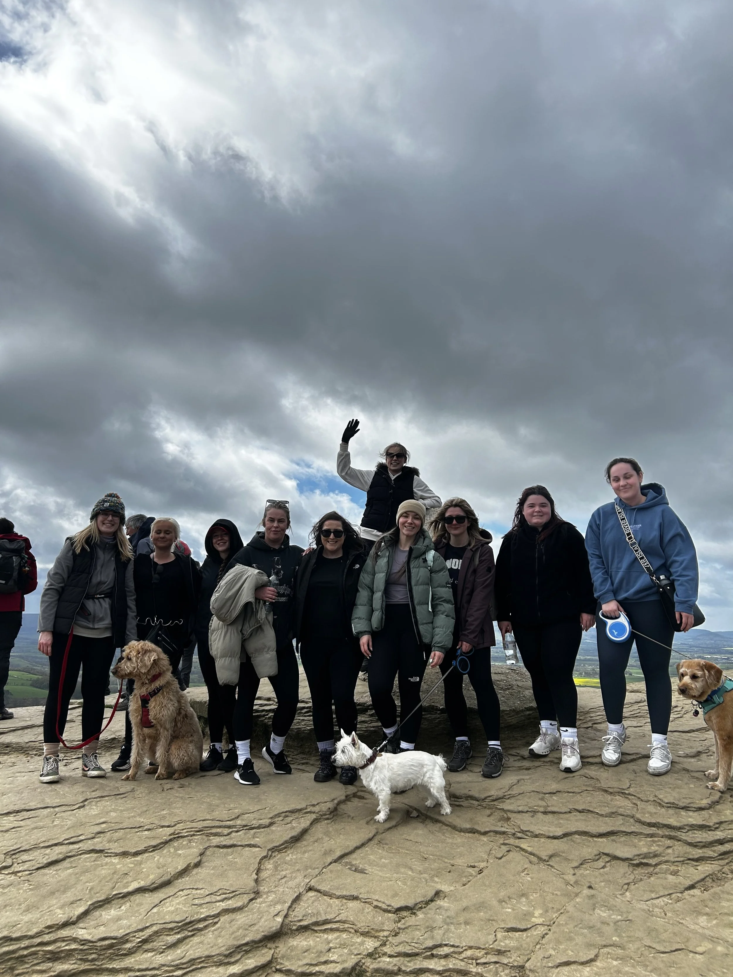 A group of people and dogs posing outdoors on a rocky surface with cloudy skies above.