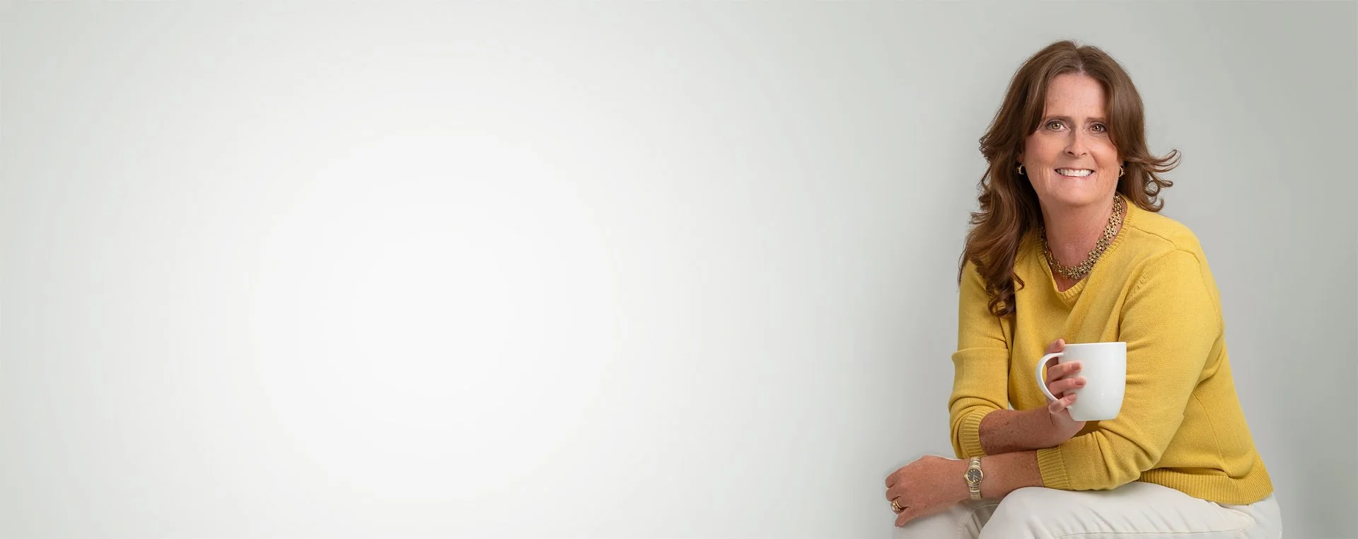 Angie Clark Consulting | Human + Resources. She is holding a white mug in her right hand, smiling at the camera, and wearing a gold necklace, earrings, and a bracelet.
