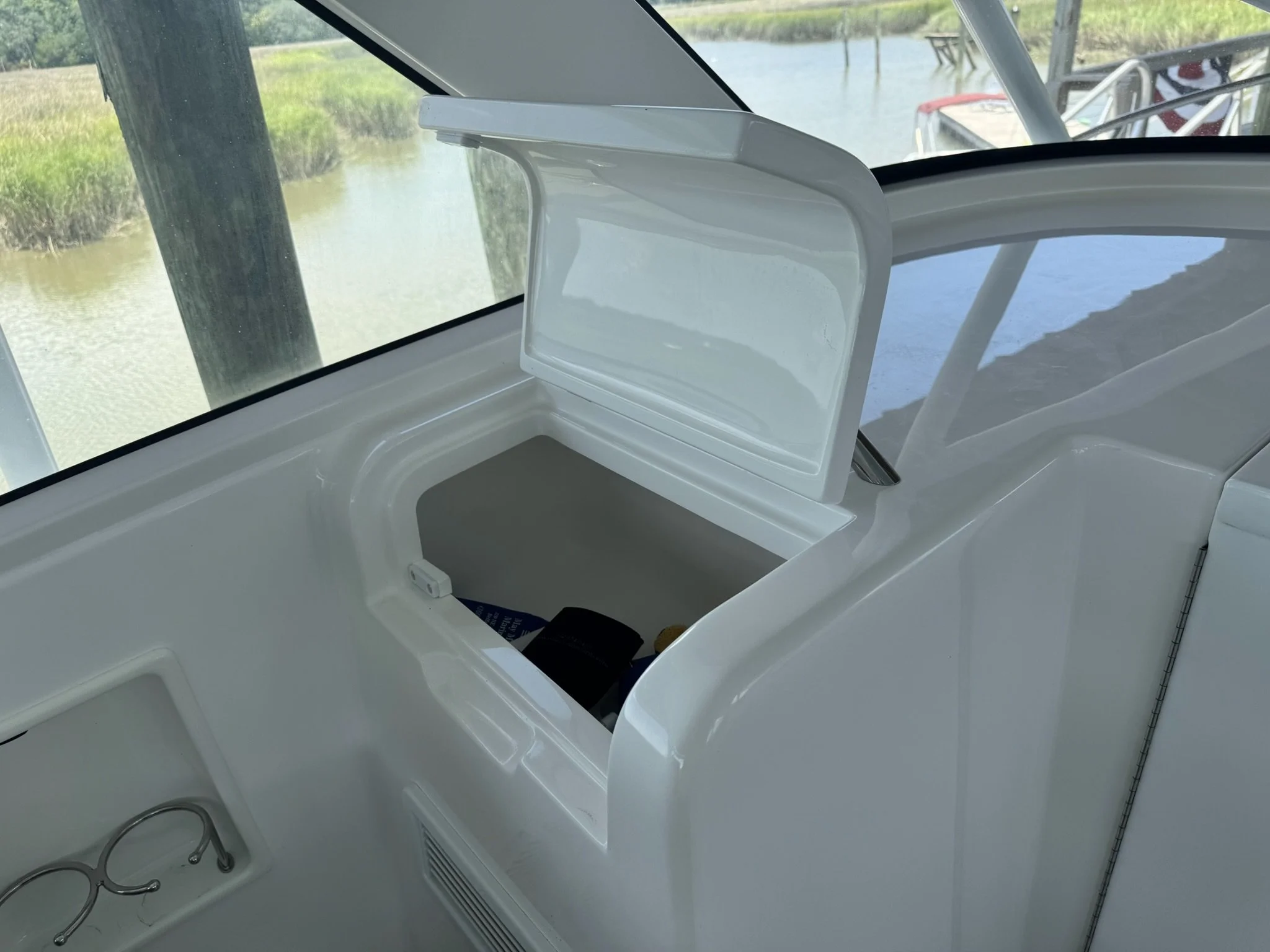 View of boat interior with a built-in small sink, situated next to a large window overlooking a waterway with grassy banks and a dock in the distance.