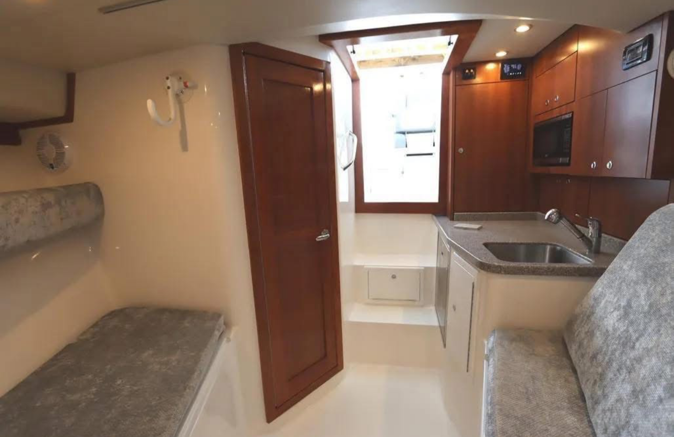 Interior of a small camper or RV with a kitchenette, wooden cabinets, a sink, and a foldable bed or seating area.