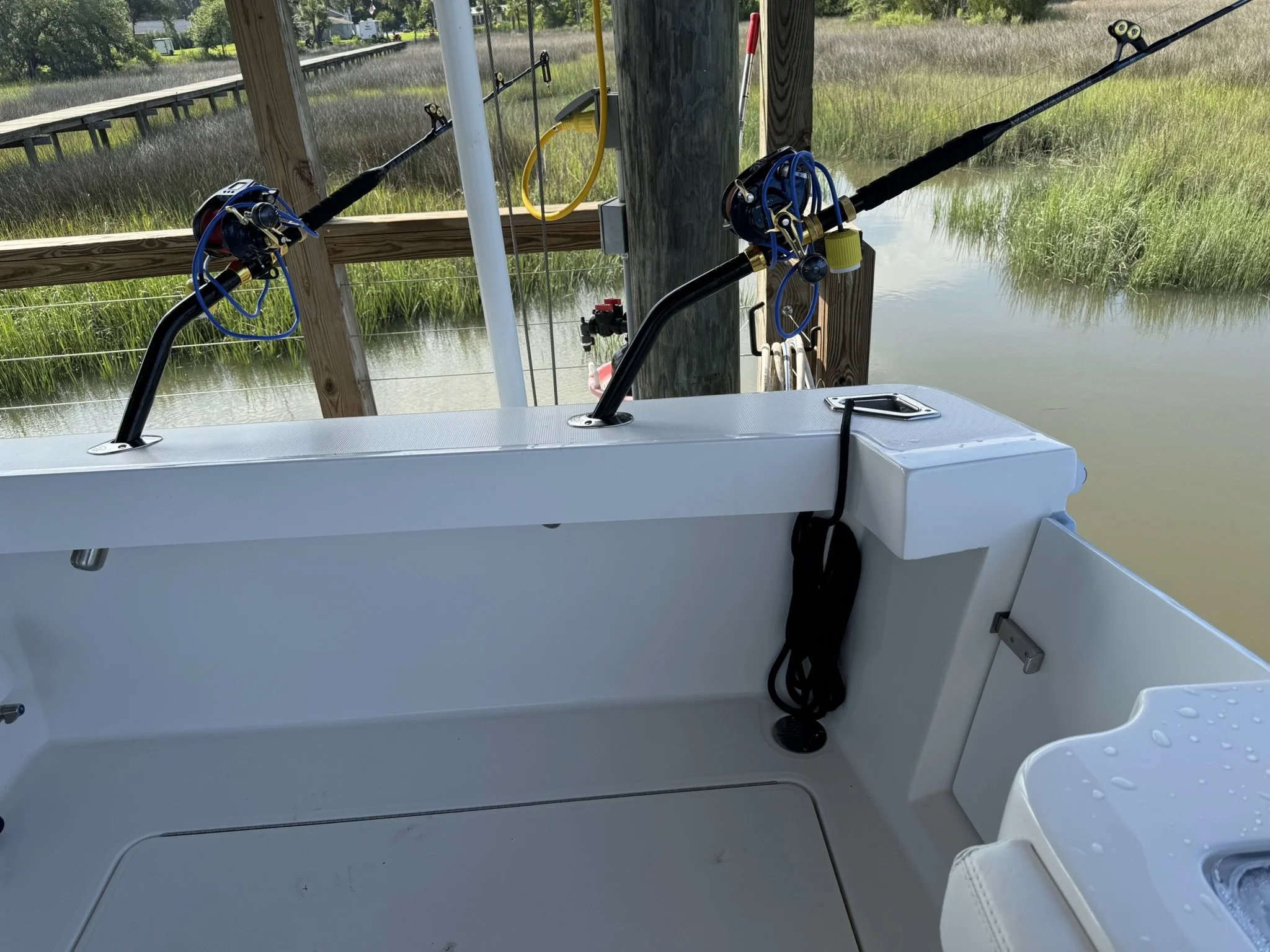 Close-up of fishing rods mounted on a boat, pointing outward over calm water with green marsh grass in the background.