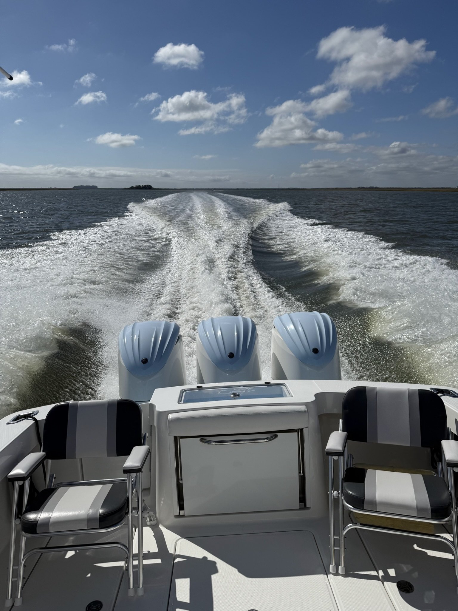 View from the back of a boat showing four outboard motors and seating area, with water and sky in the distance.