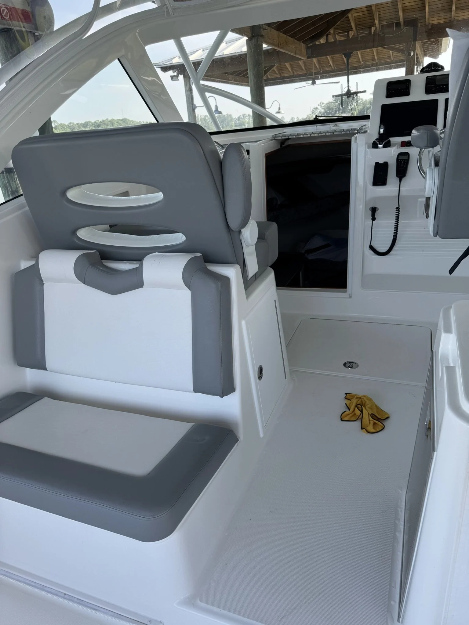 Interior of a boat with gray and white seating, a control panel with electronics, and a yellow cloth on the floor.