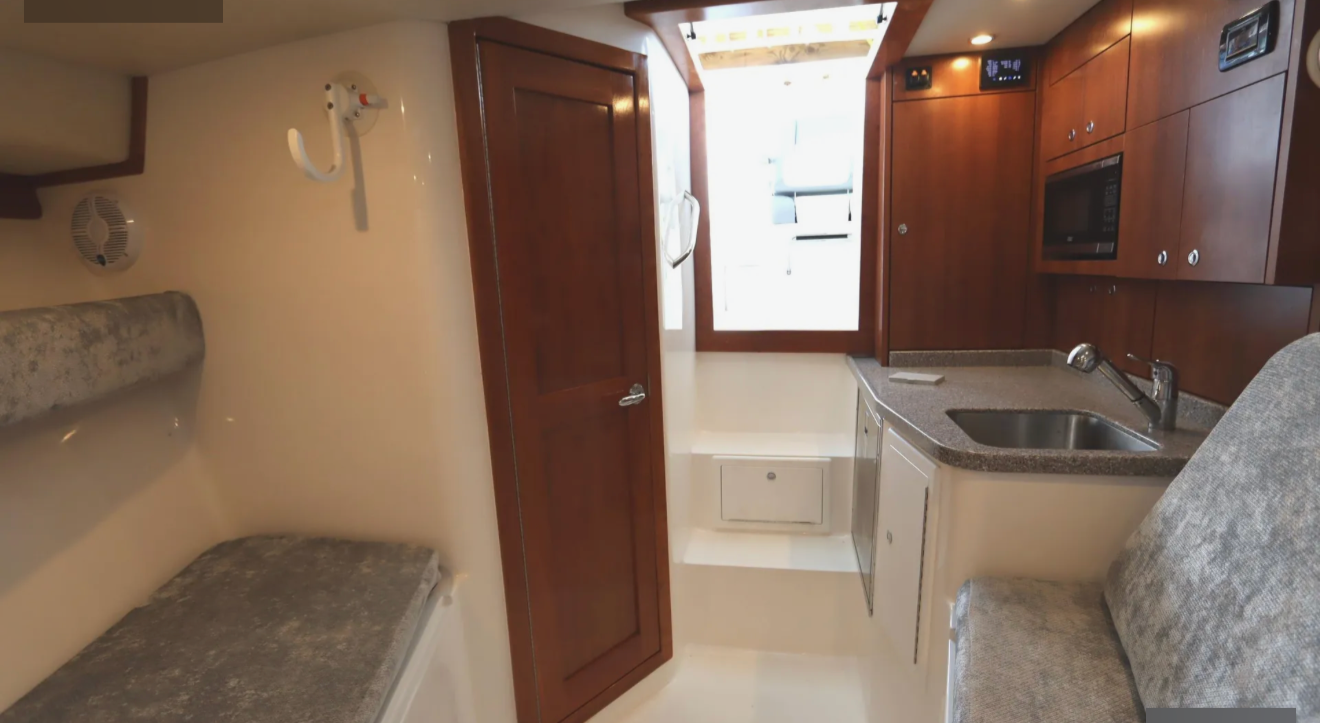 Interior of a small kitchen area with brown cabinets, a sink, a microwave, and a window letting in natural light.