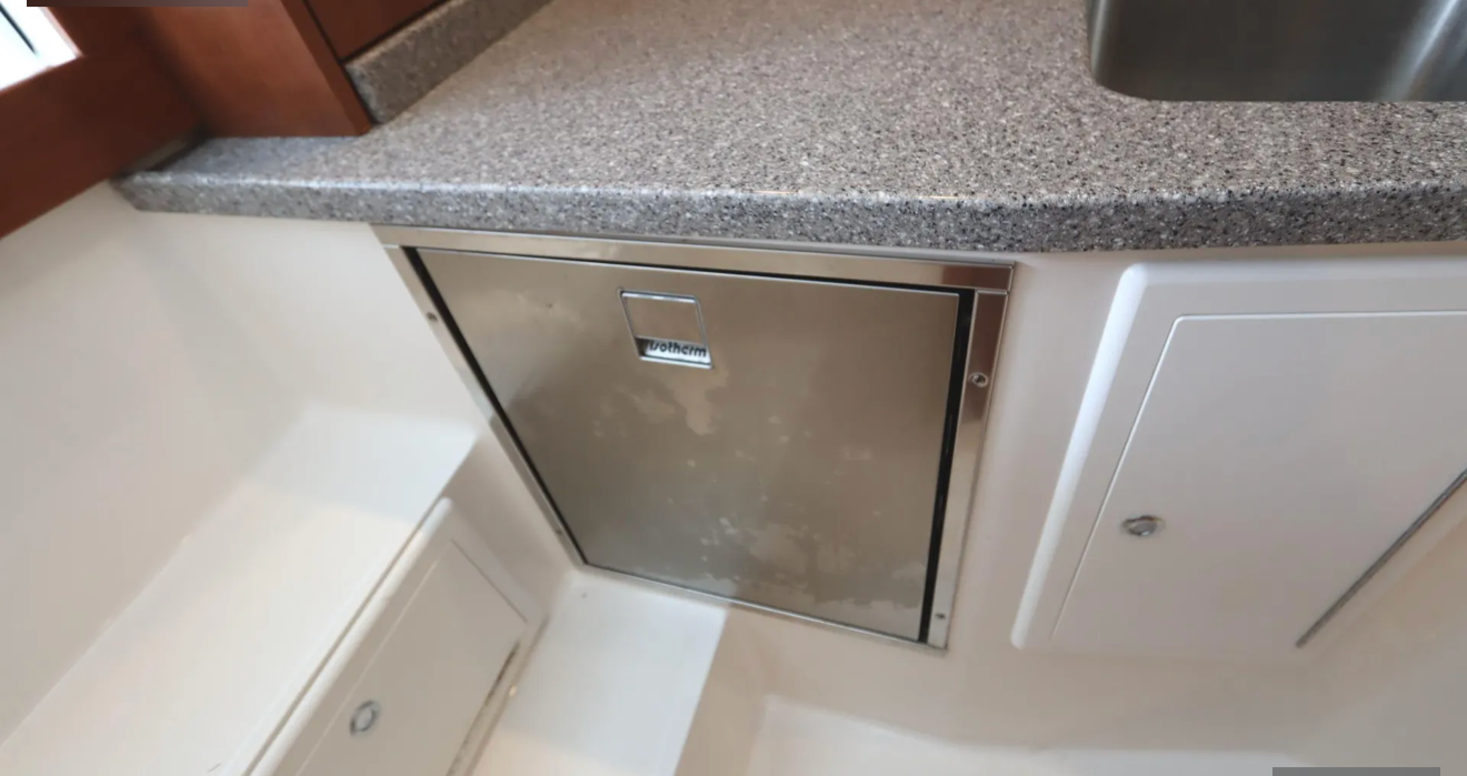 Stainless steel built-in mini fridge under a granite countertop in a kitchen.