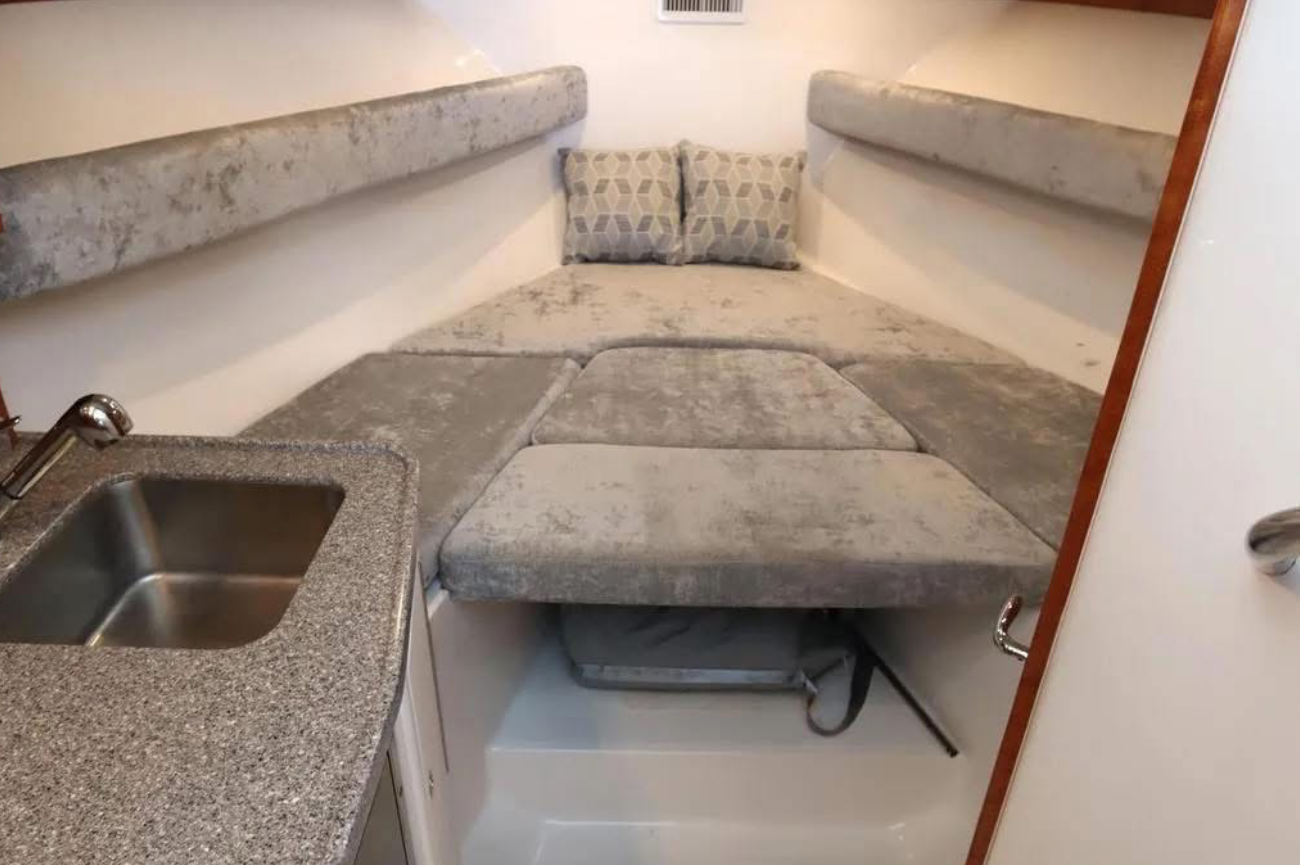 Compact living space with a small kitchen sink and a fold-out bed or sofa with cushions, in a cozy, boat or RV interior.