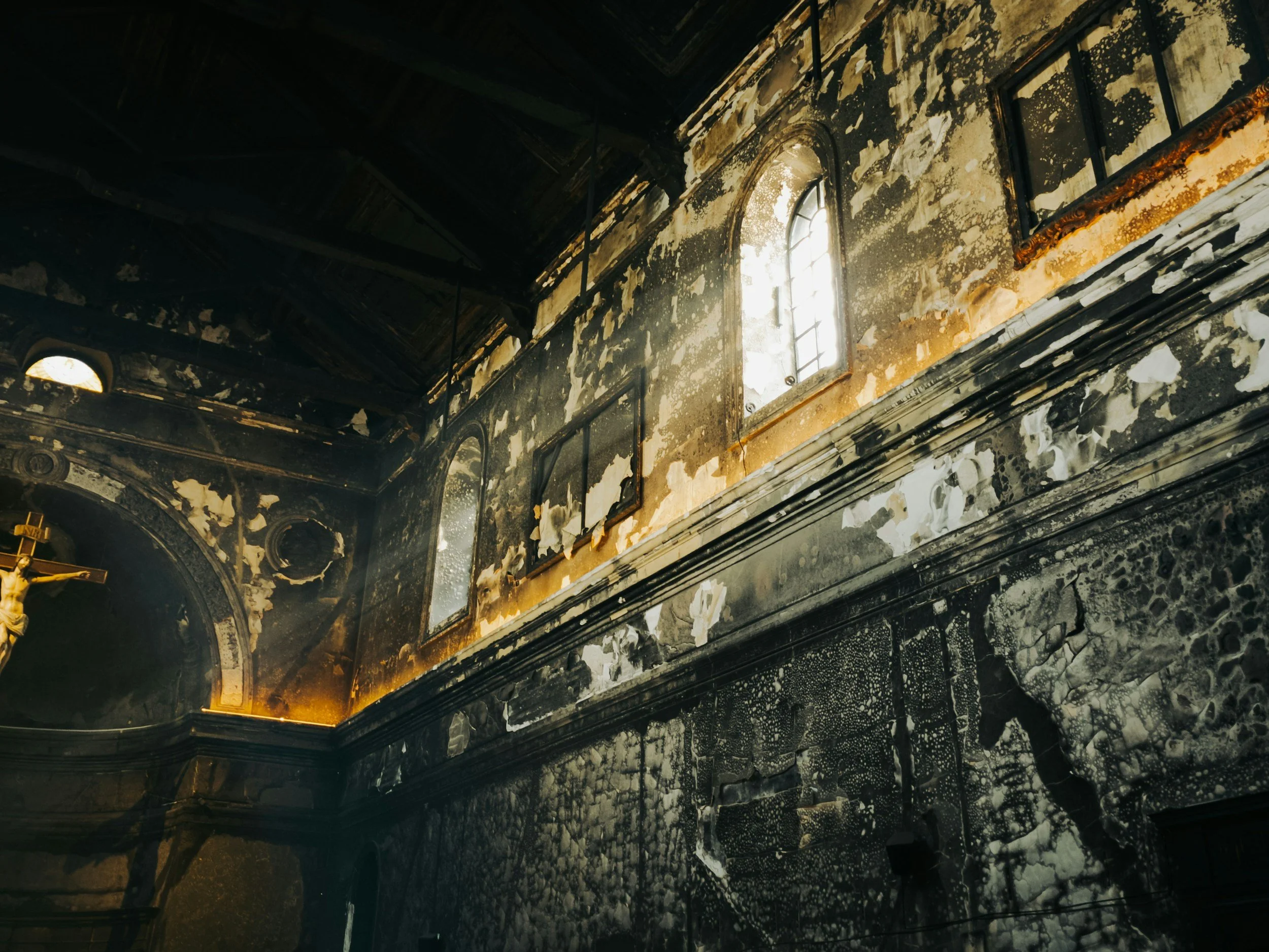 Interior of a church or cathedral with damaged and blackened walls and ceiling, stained glass windows, and ornate architectural details.
