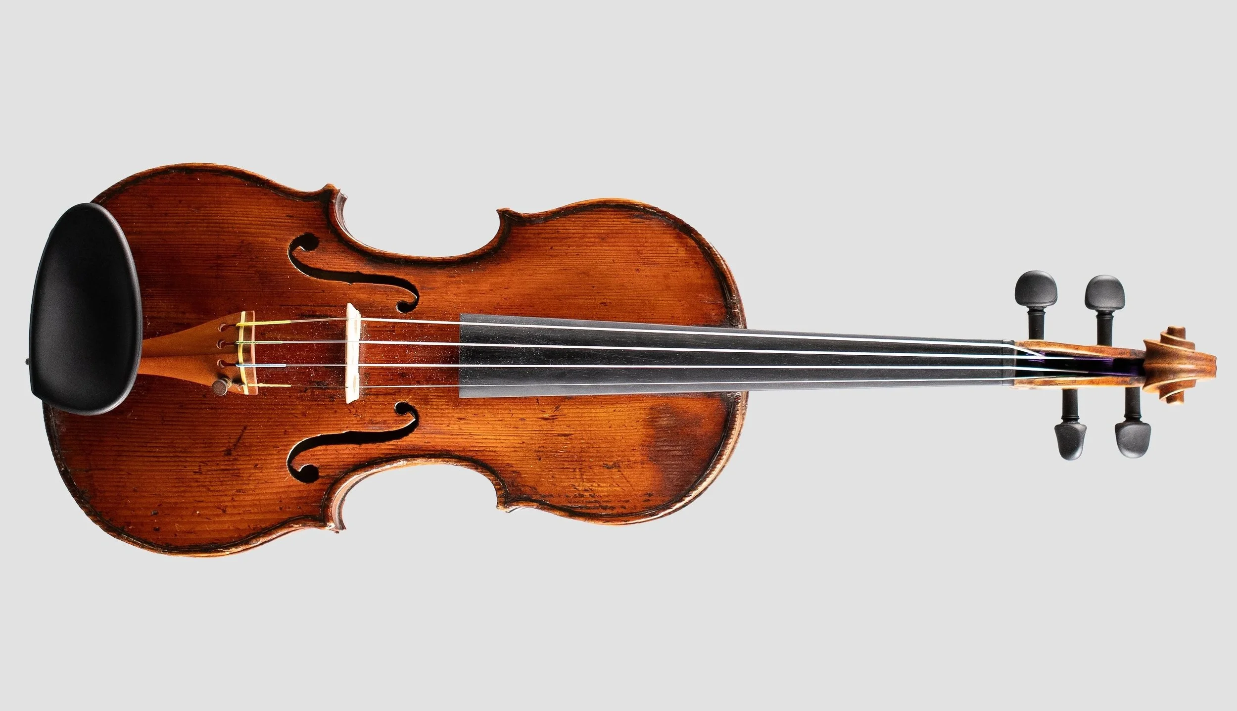 vintage wooden violin with a black chin rest, four strings, tuning pegs, and a scroll, isolated on a plain light gray background.