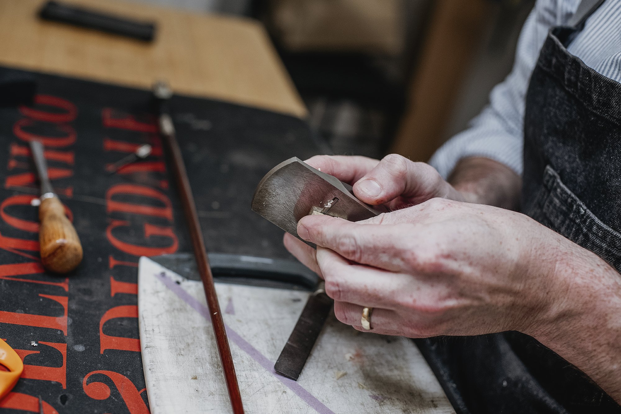 A person holding a sharpening stone or whetstone over a work surface with tools and materials nearby.