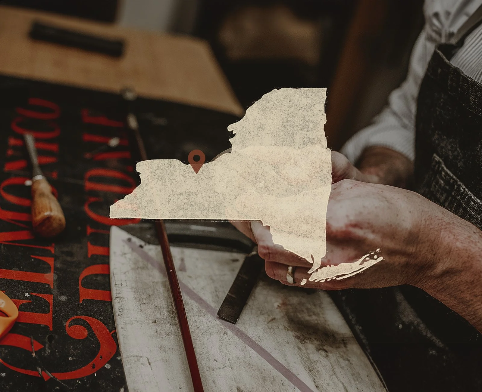 Person holding a torn paper map of the state of Maine with a location pin marking a spot.