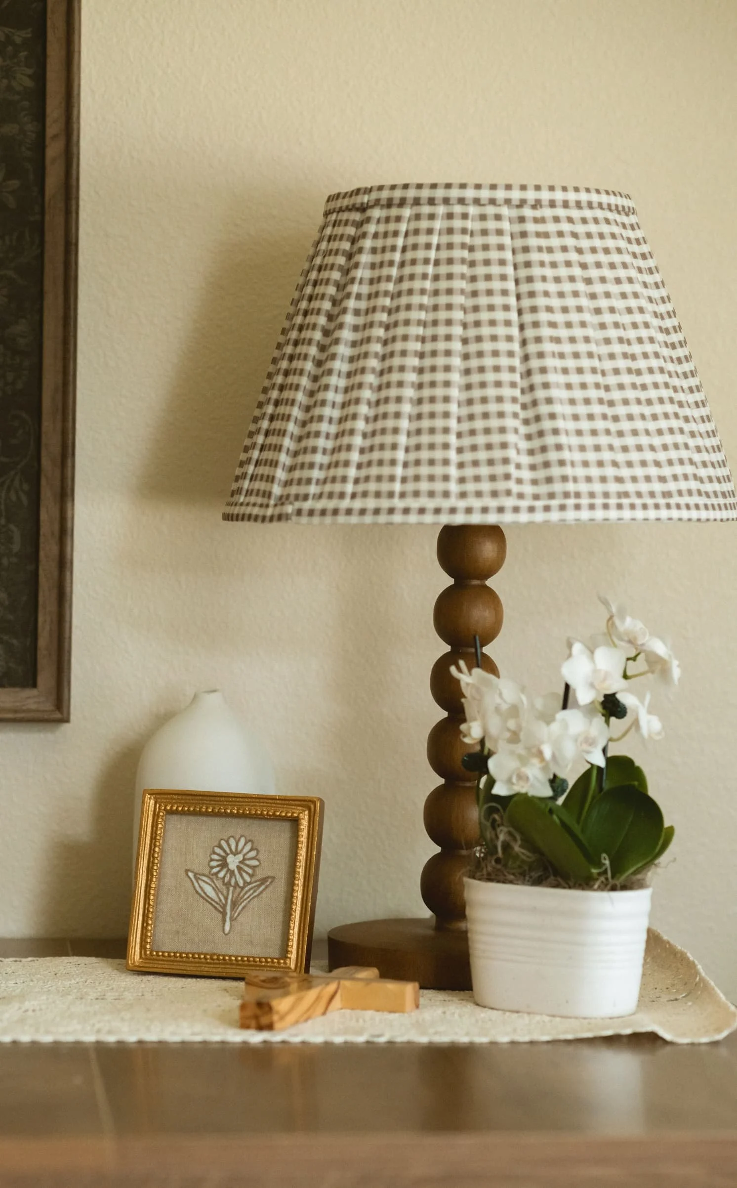 Cozy tabletop vignette with a checkered lamp, framed floral art, and orchid at The Haven