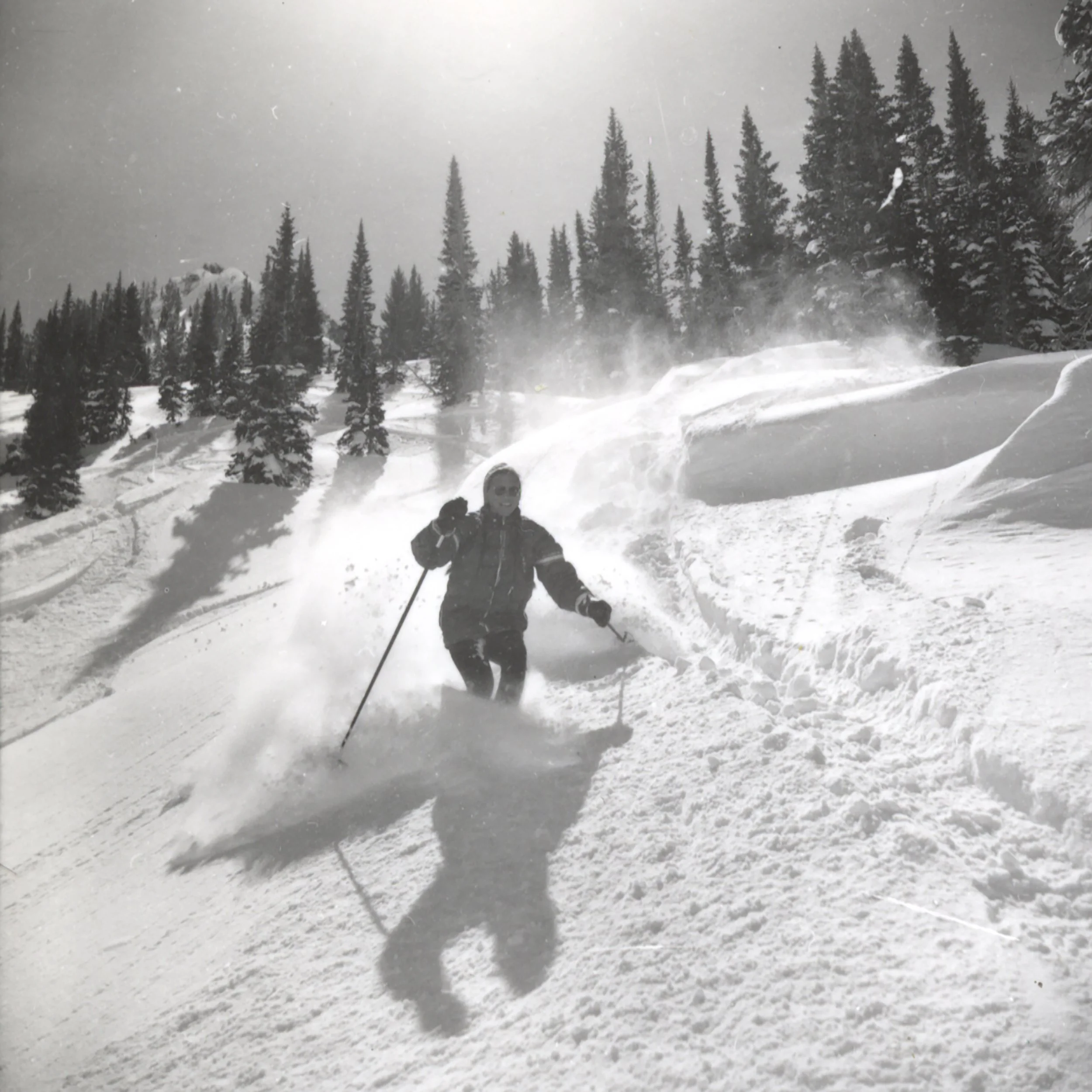 Dolores  LaChapelle completes a turn in powder snow with the sun shining behind and above her. She is smiling. Location unknown but likely Alta, Utah.