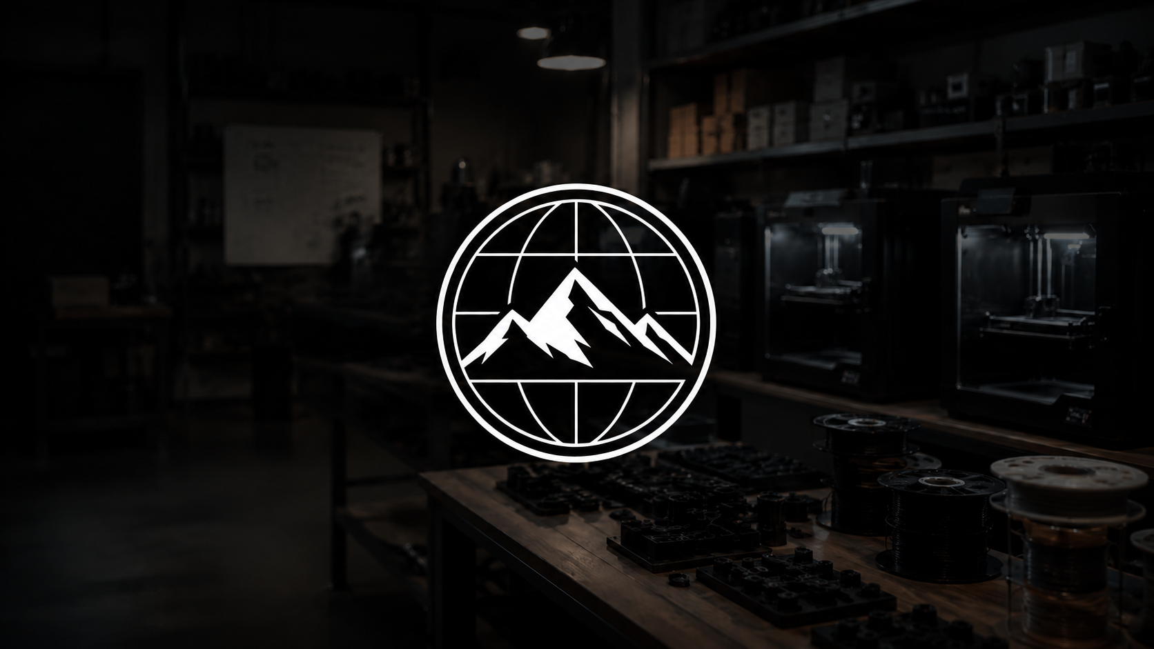 The image shows a dark workshop or studio with shelves and workbenches, illuminated by a few small light sources. In the center, a bright, white, minimalist logo of mountain peaks inside a globe outline is prominently displayed.