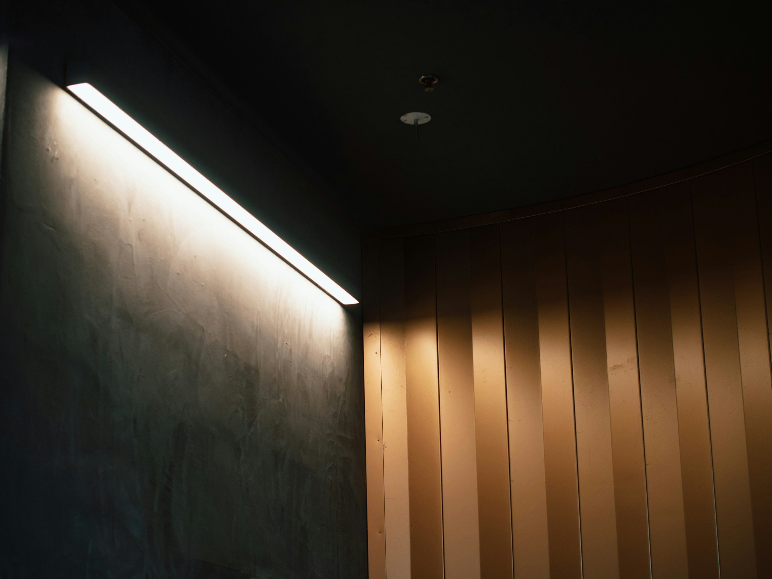 Un mur sombre avec une ligne de lumière blanche et une rangée de panneaux en bois éclairés doucement.
