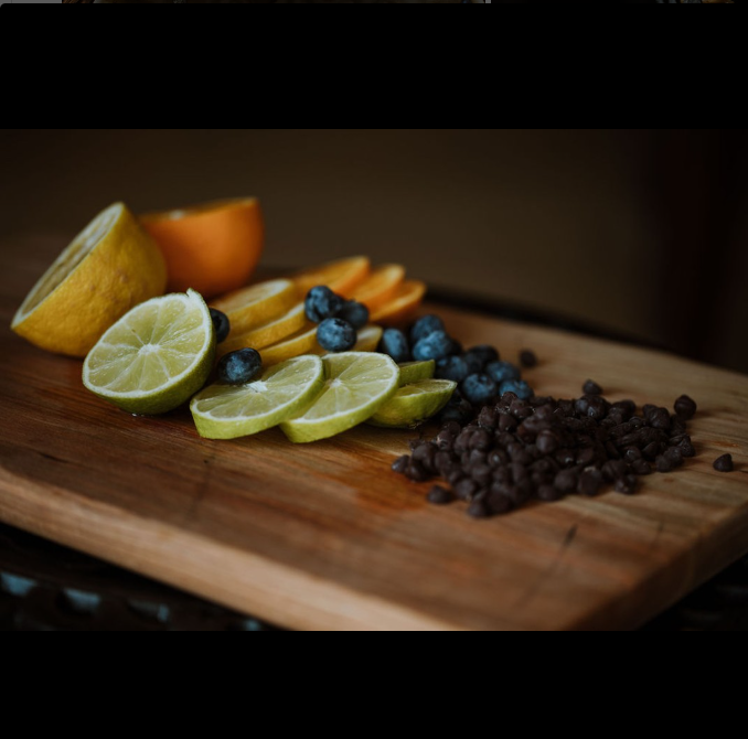 Assorted sliced citrus fruits, blueberries, and chocolate chips on a wooden cutting board.