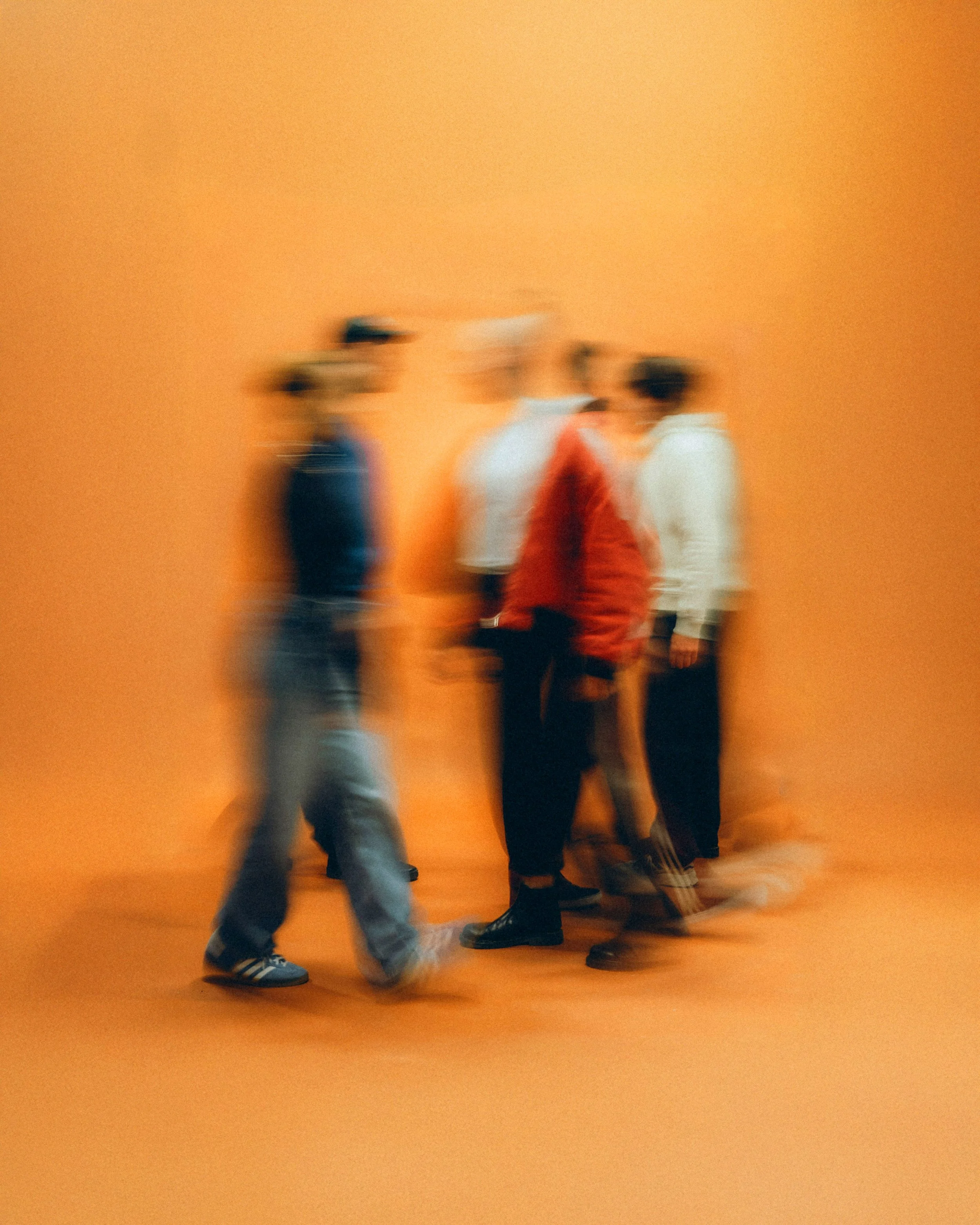 Four people walking in front of an orange wall, two women and two men, with the image intentionally blurred.