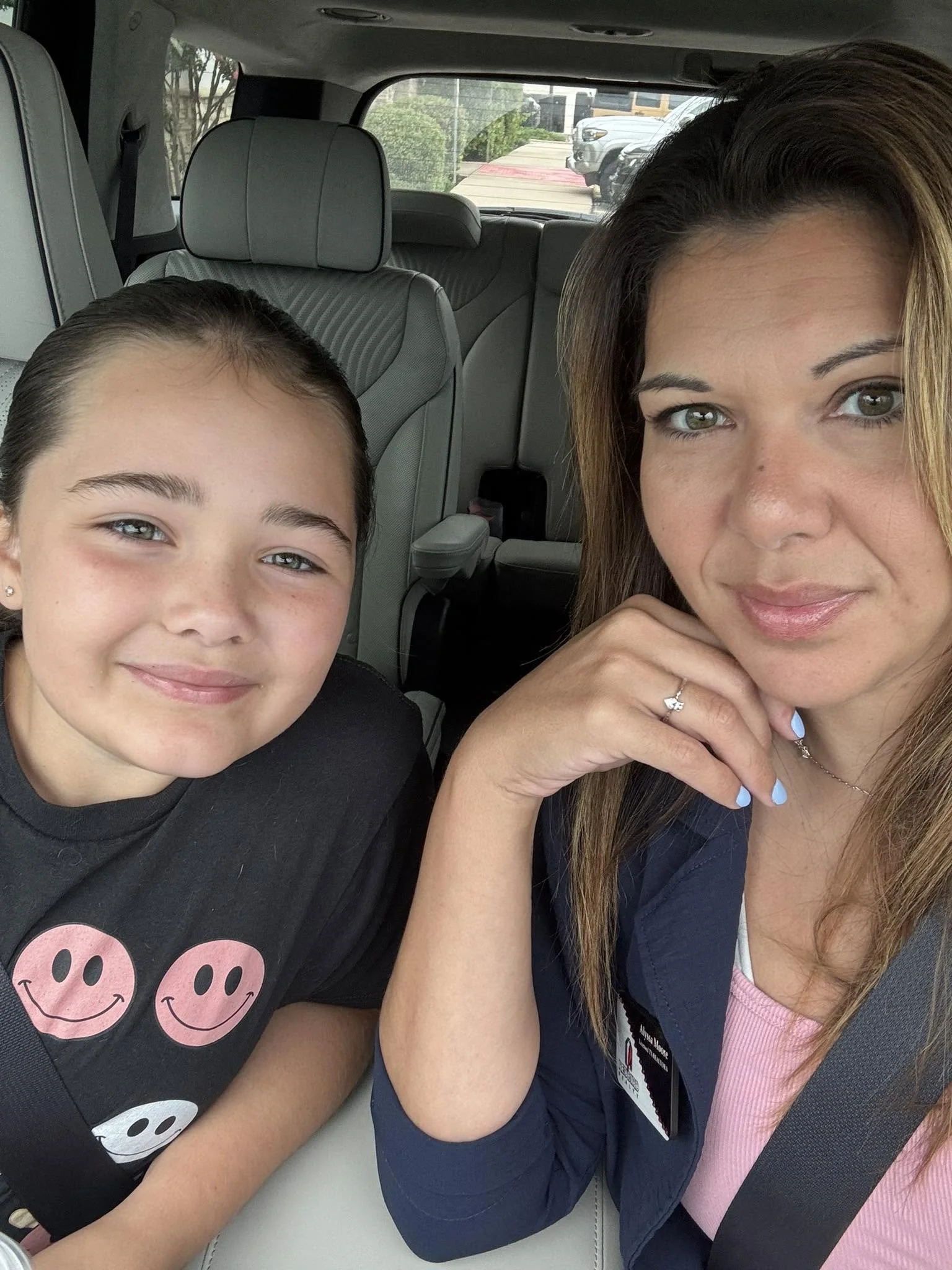 A woman and a young girl sitting in a car, smiling at the camera.
