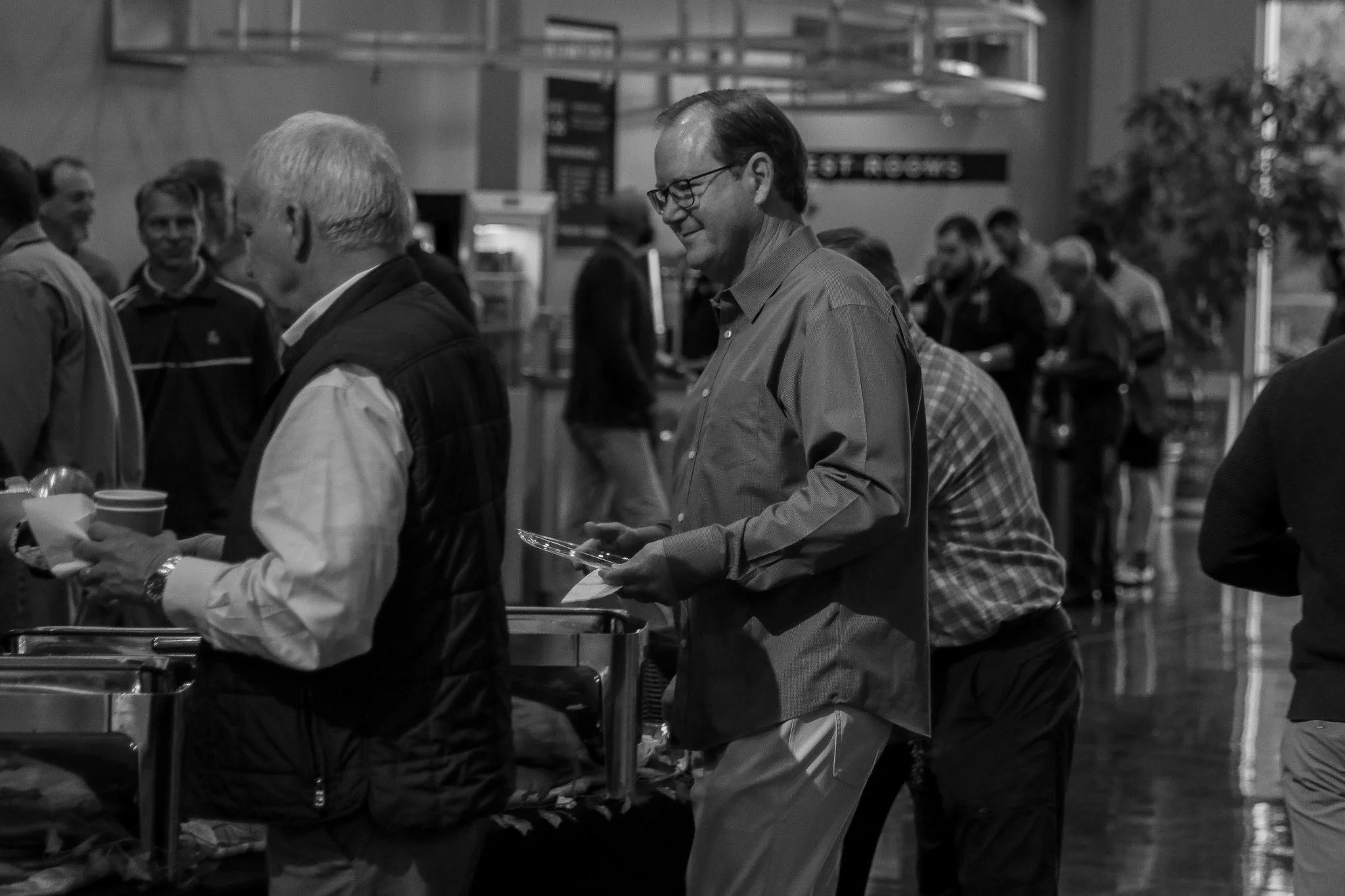 People in line at a breakfast buffer, with some holding plates.