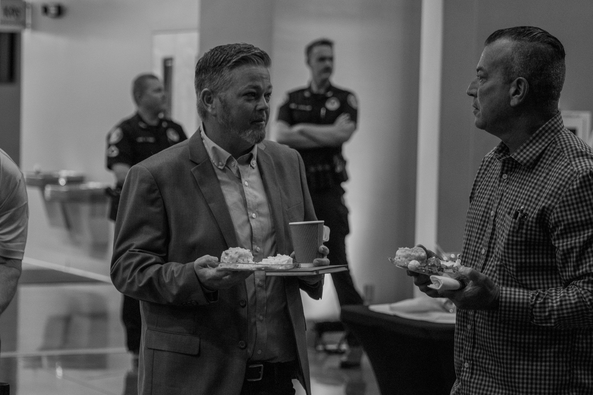 Two men are engaged in conversation while holding trays of food; with two others standing in the background.