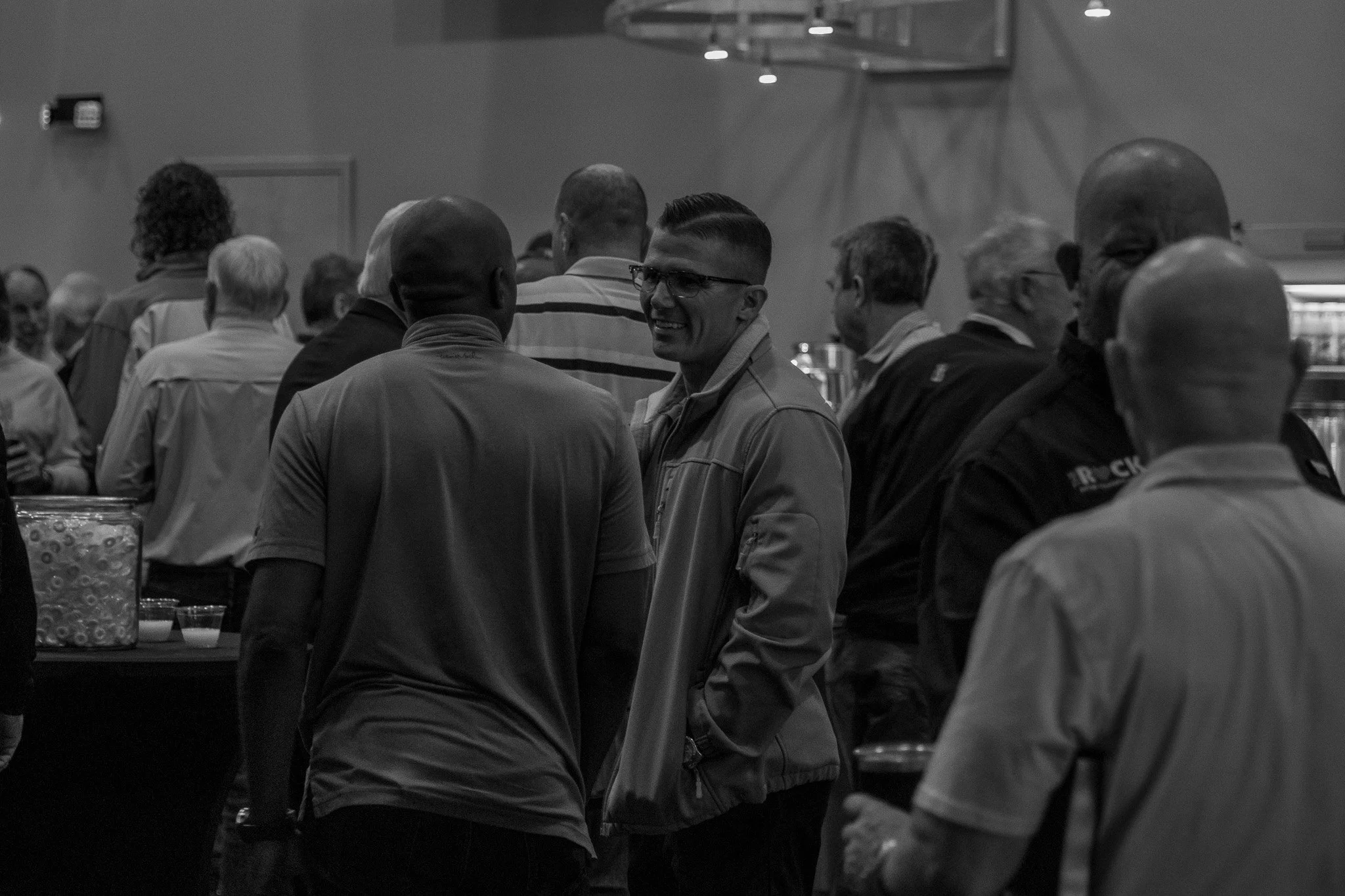 People gathered at a social event, engaging in conversation and smiling, in a large indoor space.