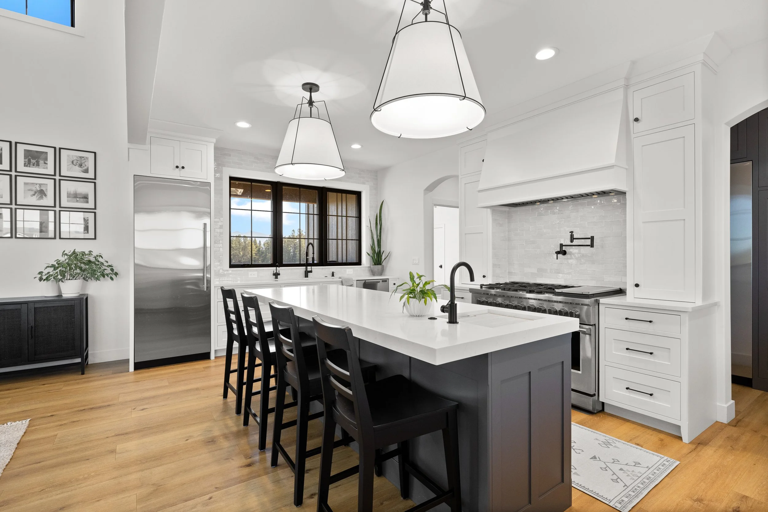 Bright white kitchen with dark island, bar stools, and large pendant lights — LR Studio interior design Connecticut