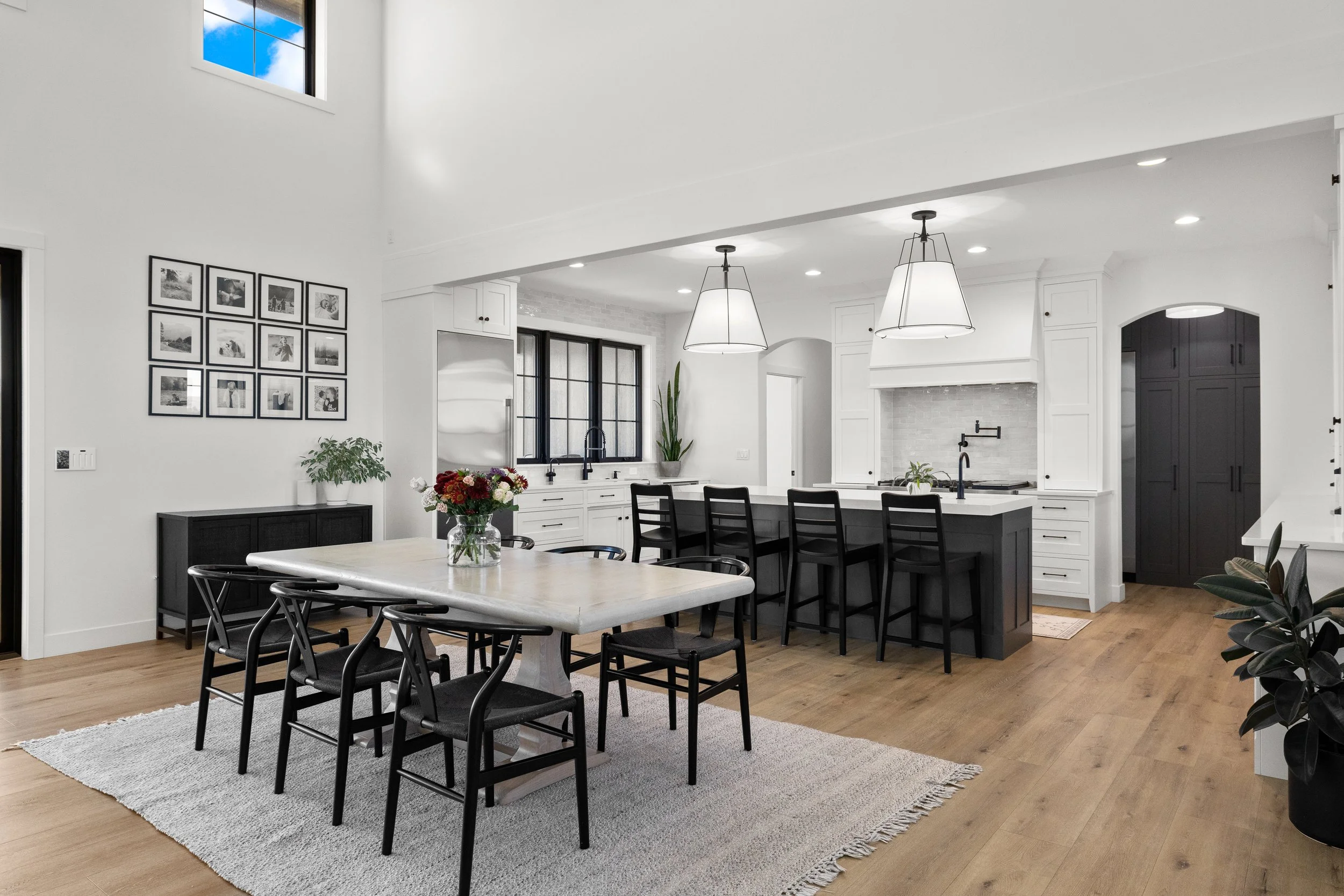 Open-concept kitchen and dining area with dark island, pendant lighting, and vaulted ceiling — LR Studio design