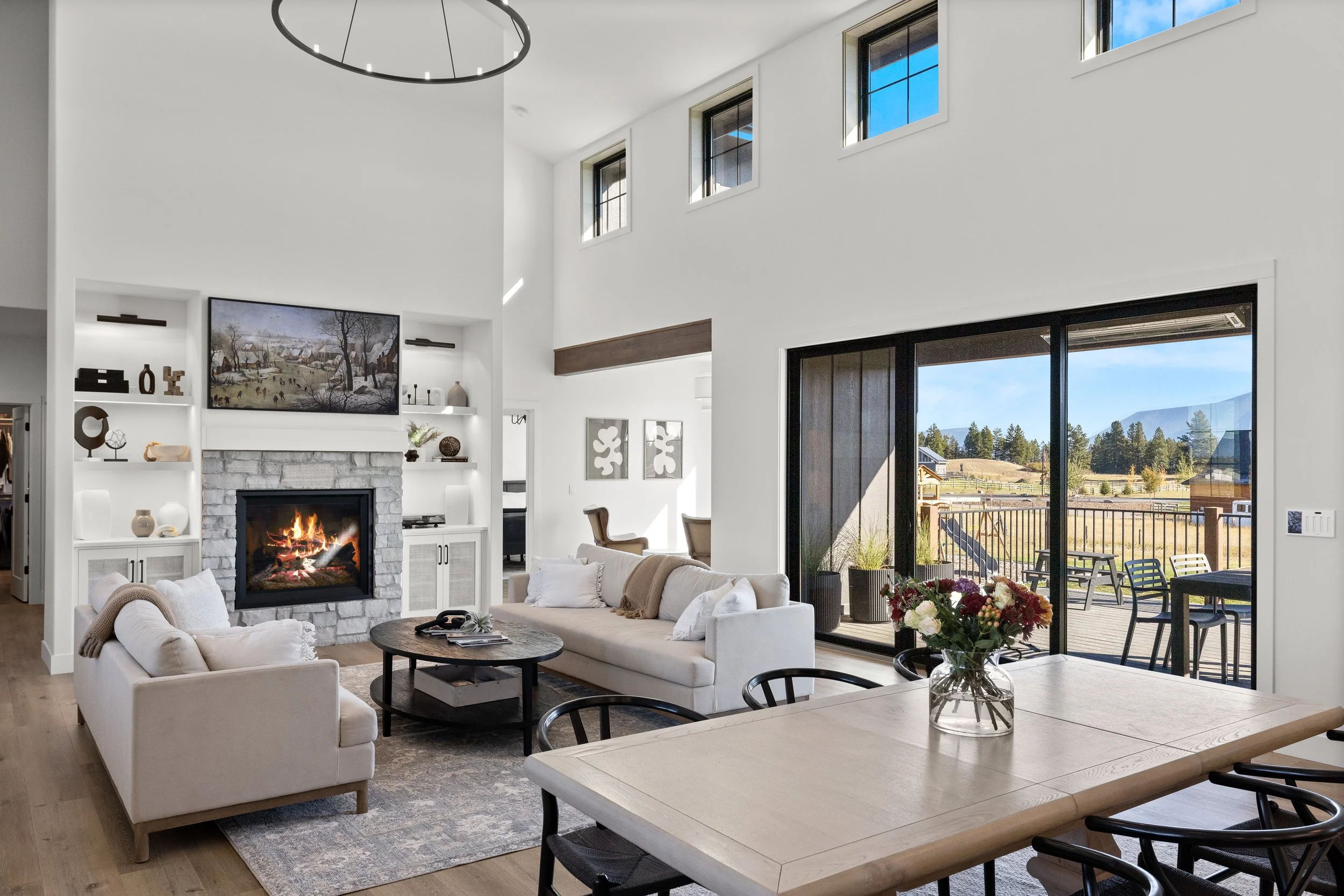Open living and dining space with stone fireplace, tall ceilings, and mountain view windows — LR Studio design