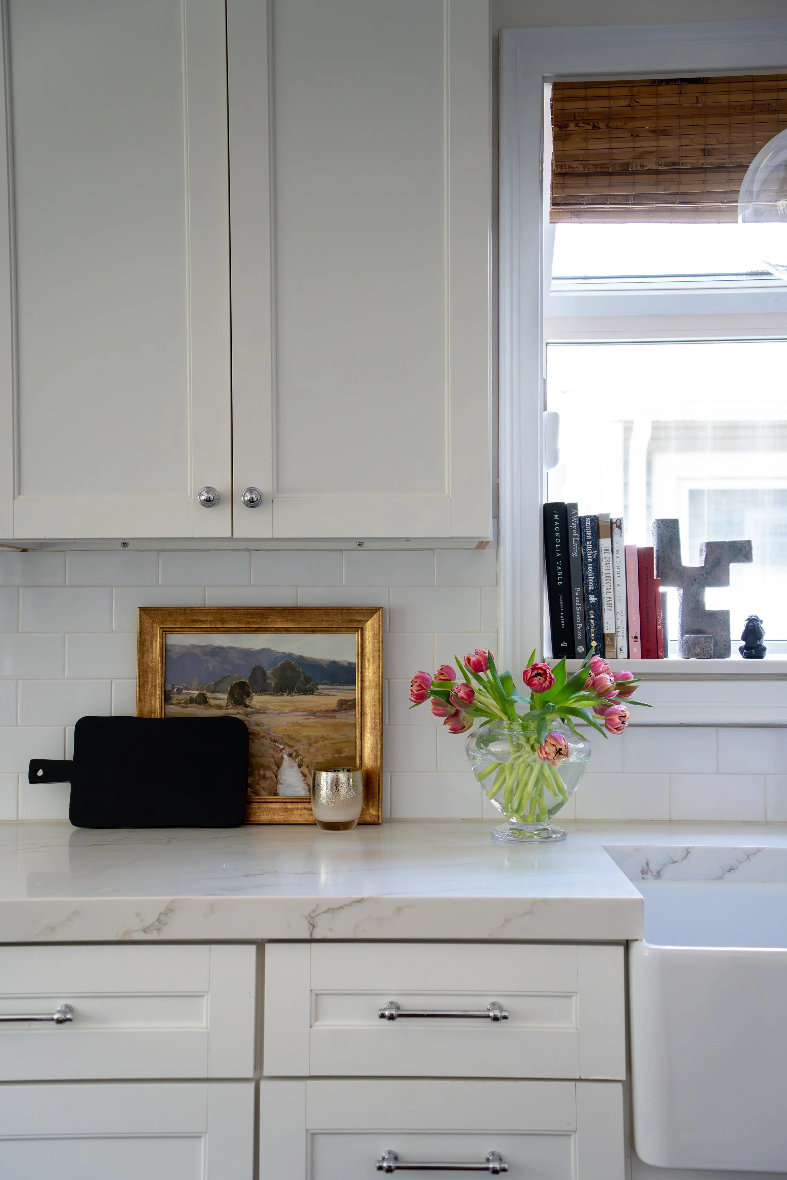 Styled kitchen vignette with framed art, fresh tulips, and decorative objects on marble counter — LR Studio