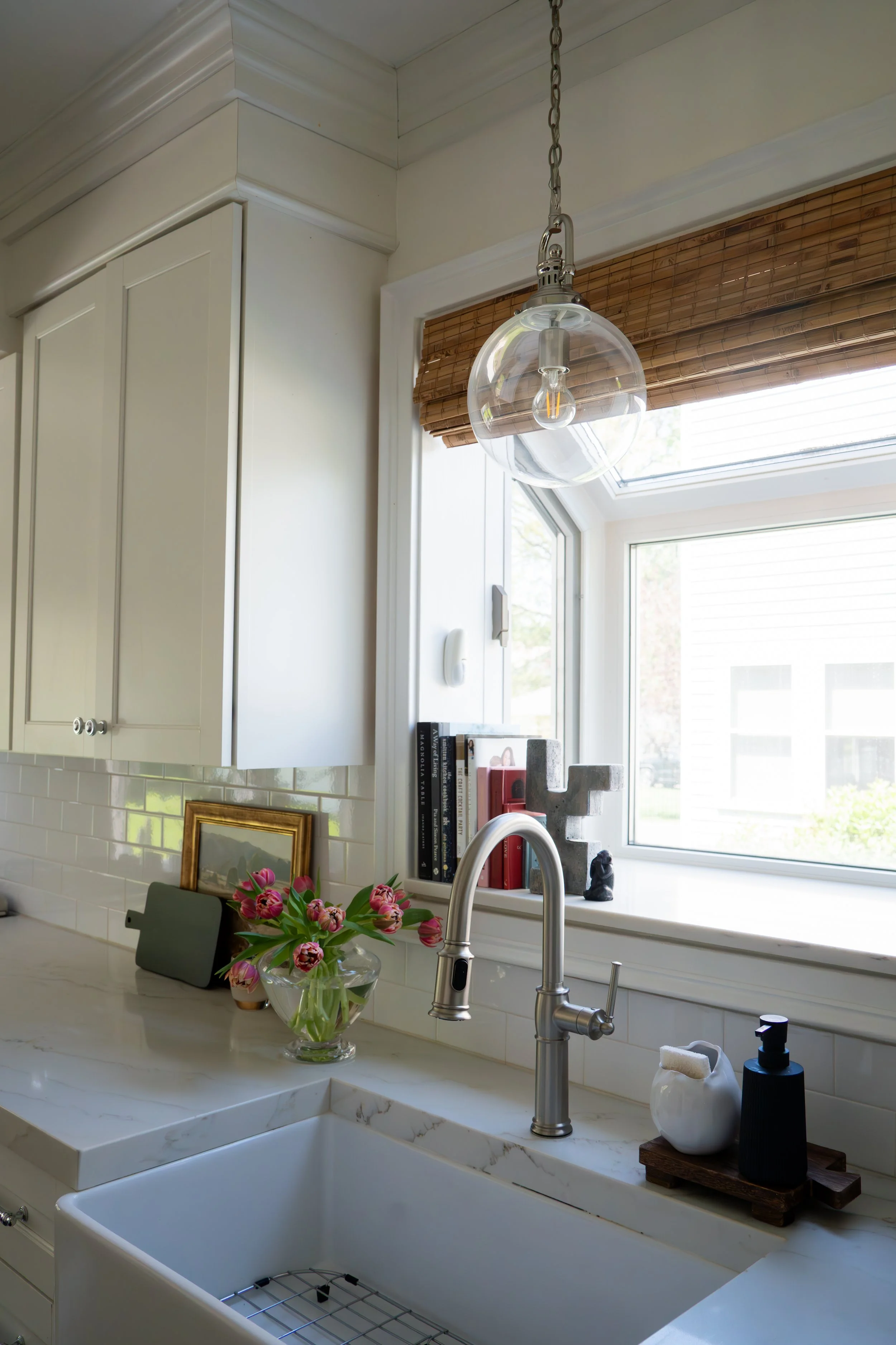 White farmhouse kitcheTransitional sitting room with neutral linen armchair, framed art, and natural light — LR Studio design Connecticutn sink with pendant light, wood shelving, and window view — LR Studio home design