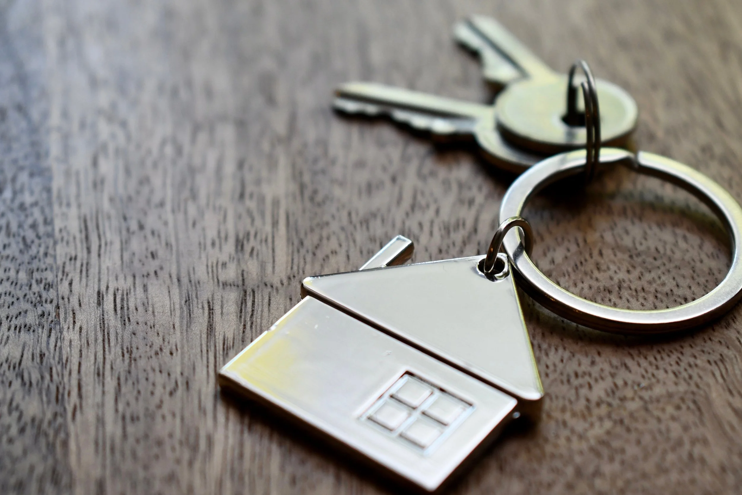 Set of metallic key with a gold finish attached to a decorative metallic keychain with a star-shaped charm, resting on a dark wooden surface.