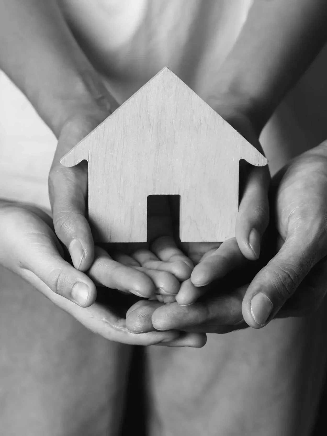 Black and white photo of two pairs of hands holding a wooden house-shaped cutout.