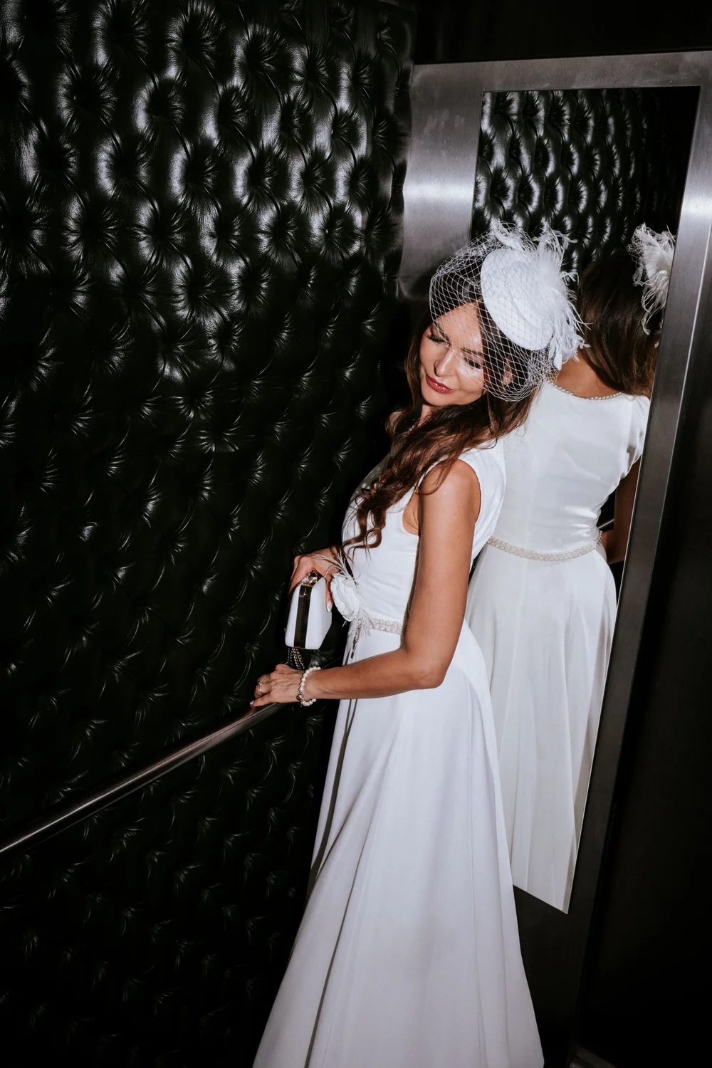 Braut mit Fascinator und Clutch im Lift des Hotels Grand Ferdinand in Wien, Blick über die Schulter