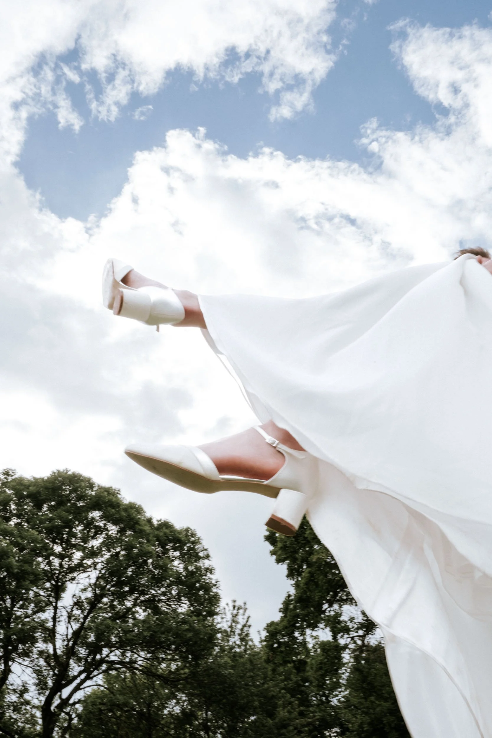 Brautschuhe und wehendes Brautkleid vor blauem Himmel, Braut wird bei der Hochzeit im Wienerwald getragen