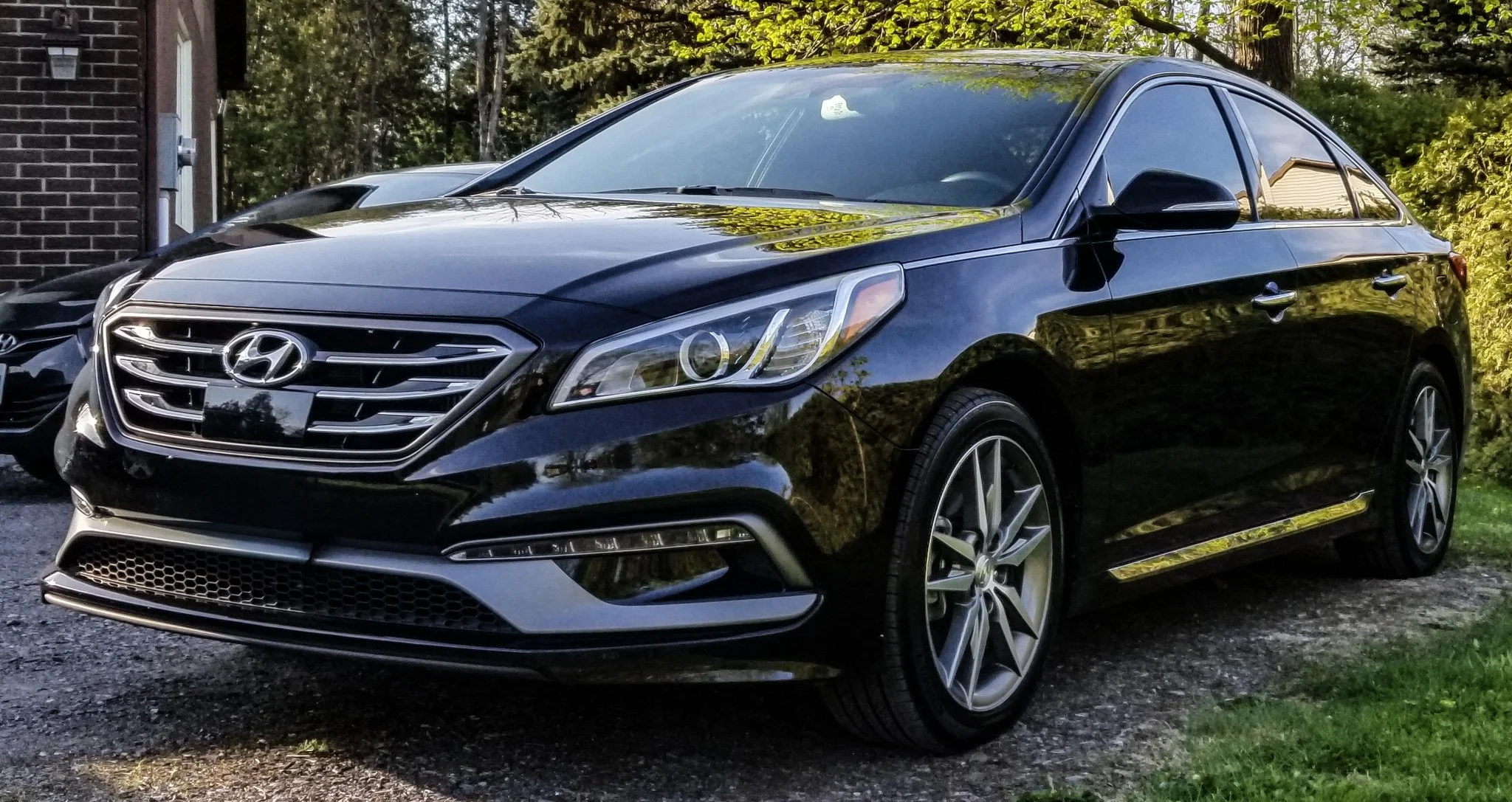Black Hyundai sedan parked outdoors near a brick building with trees and greenery in the background.