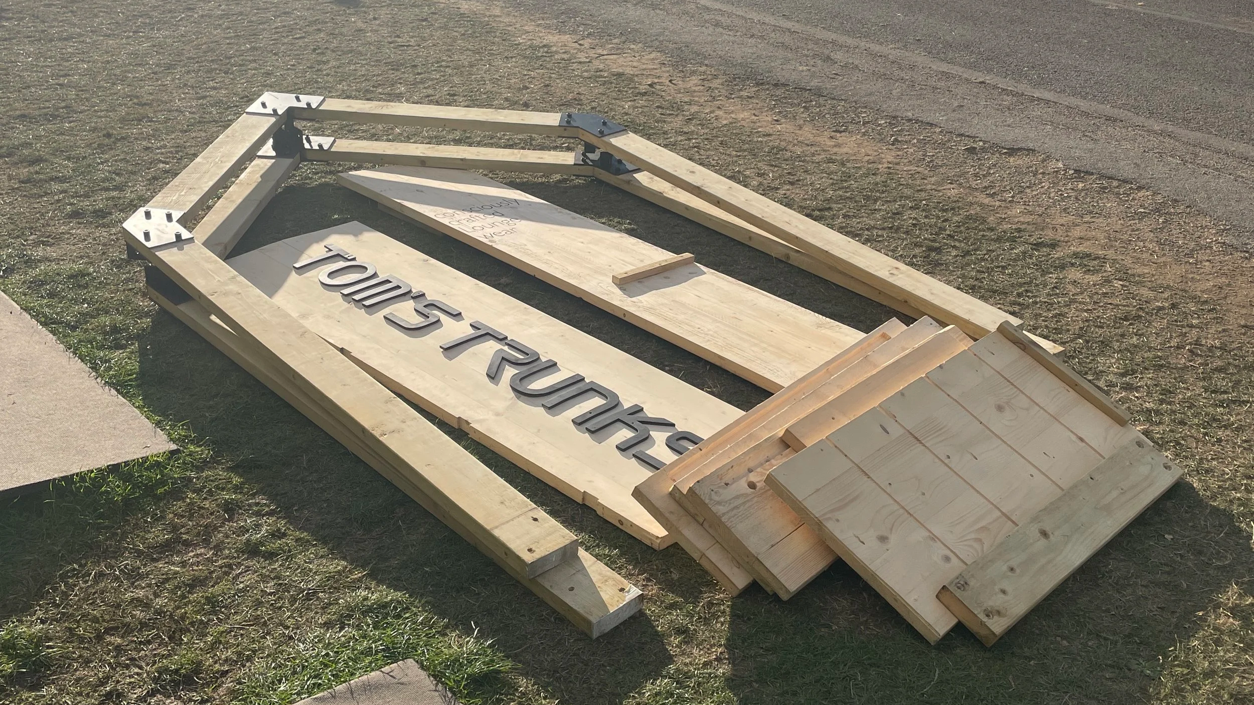 Wooden sign frame lying on the grass with a partially visible sign that reads 'TOUR TRUCKS' and some additional handwritten notes.