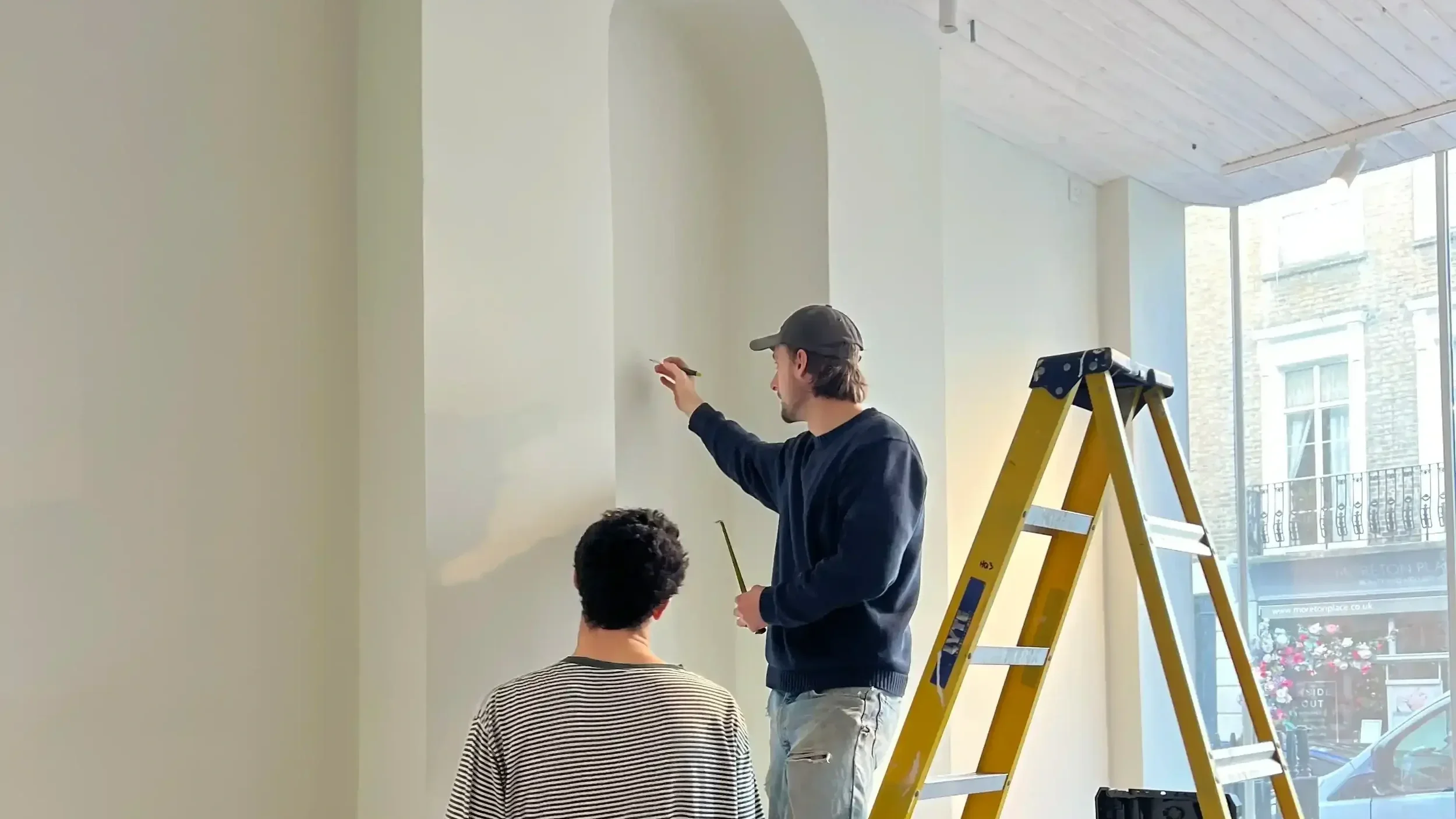 Bespoke retail fit-out in progress with two craftspeople finishing an arched alcove installation using a yellow ladder
