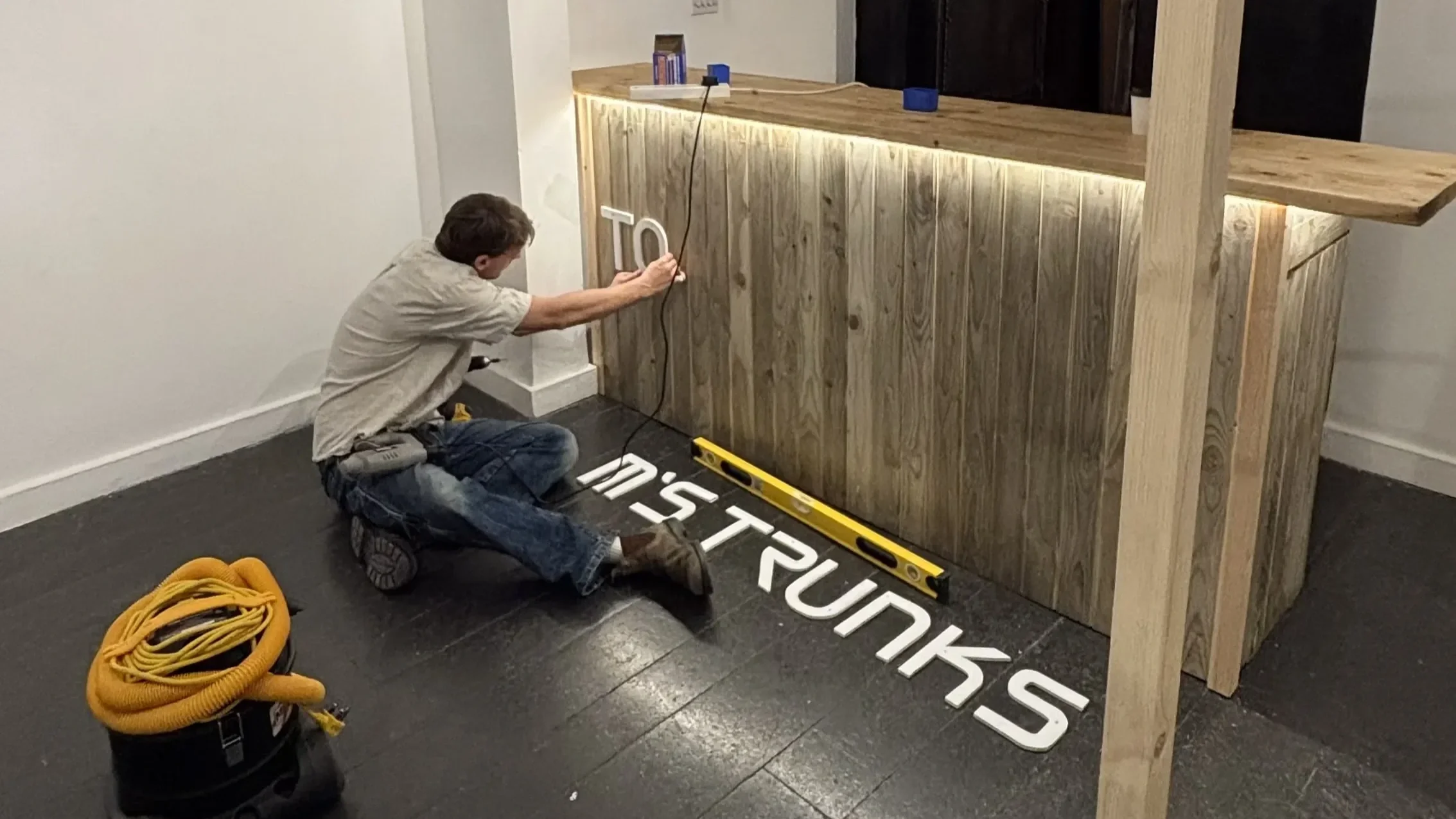 Tom's Trunks bespoke branded counter being installed in retail fit-out at night with worker on floor and track lighting above