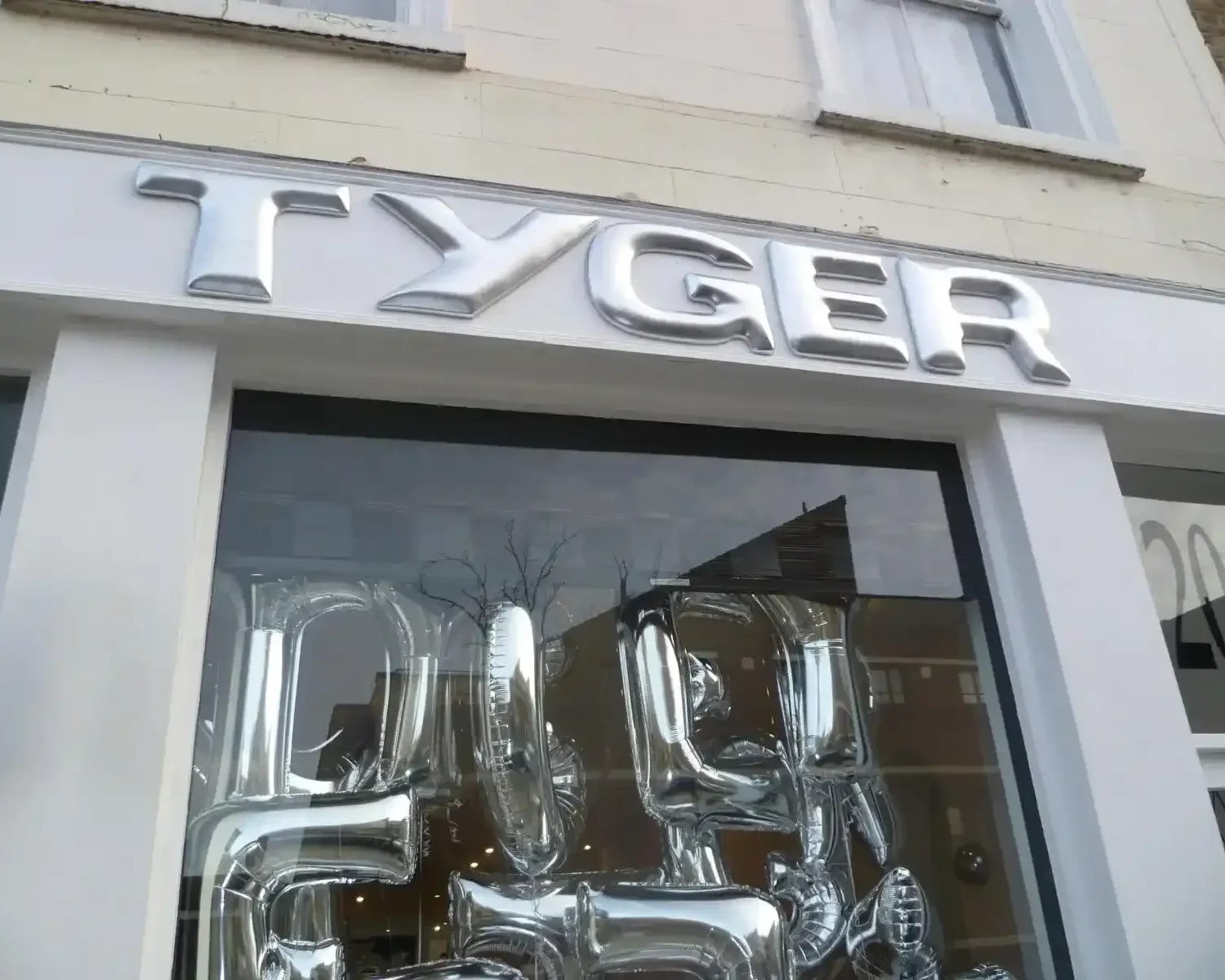 Close-up of Tyger pop-up store chrome 3D signage and silver mylar balloon window display on white London shopfront
