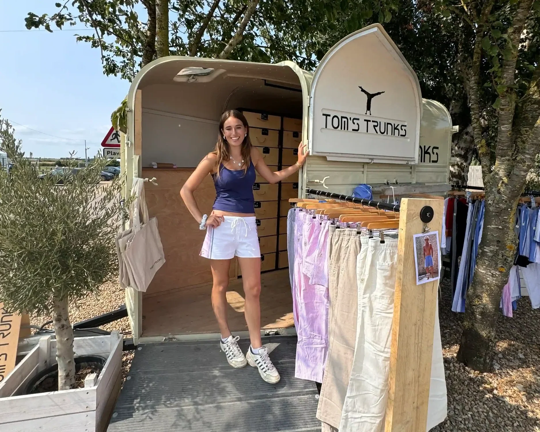 Woman at Tom's Trunks branded horsebox mobile retail brand activation unit at outdoor event on a sunny day